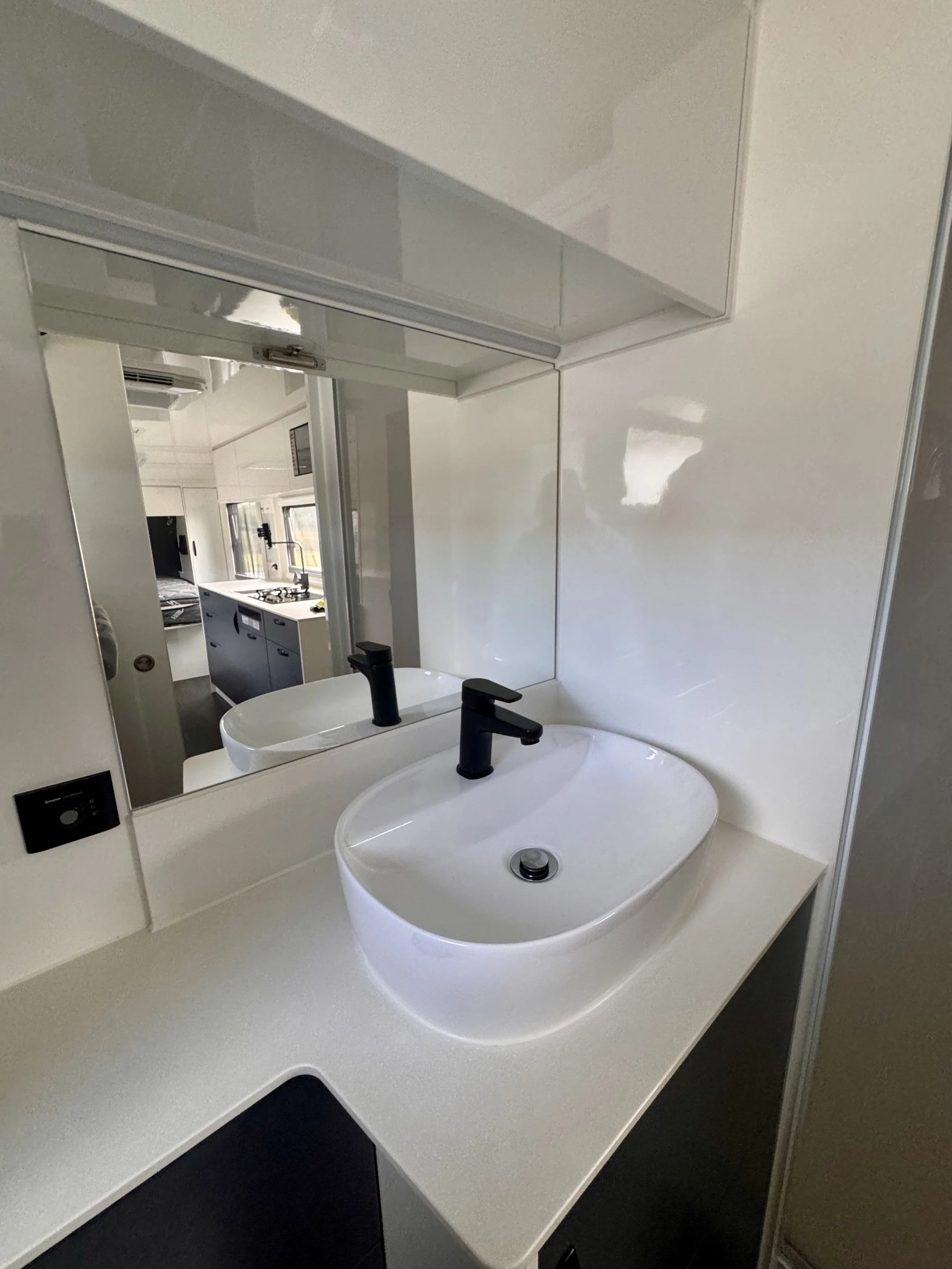 Close-up of a bathroom sink with a black faucet, a mirror, and part of a countertop in a modern, minimalist style.
