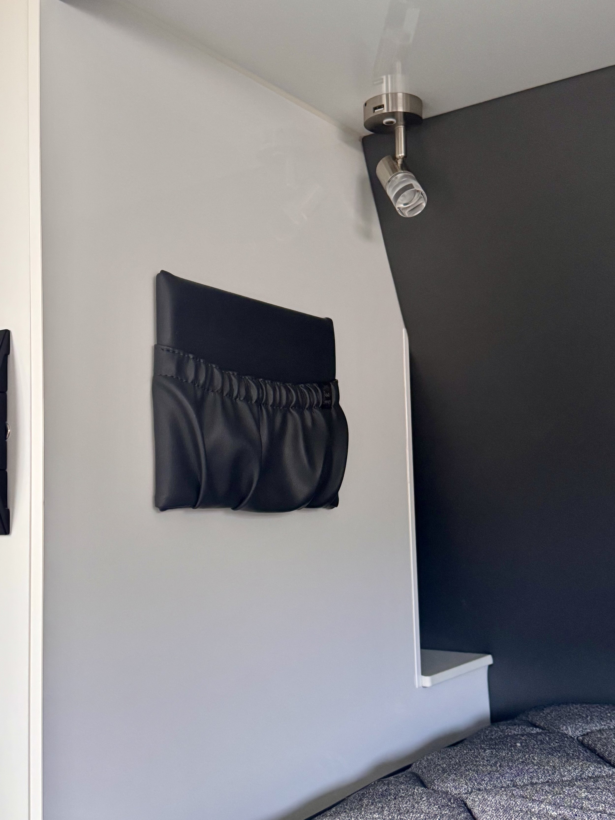 A black storage pocket hanging on a white wall next to a bed. 