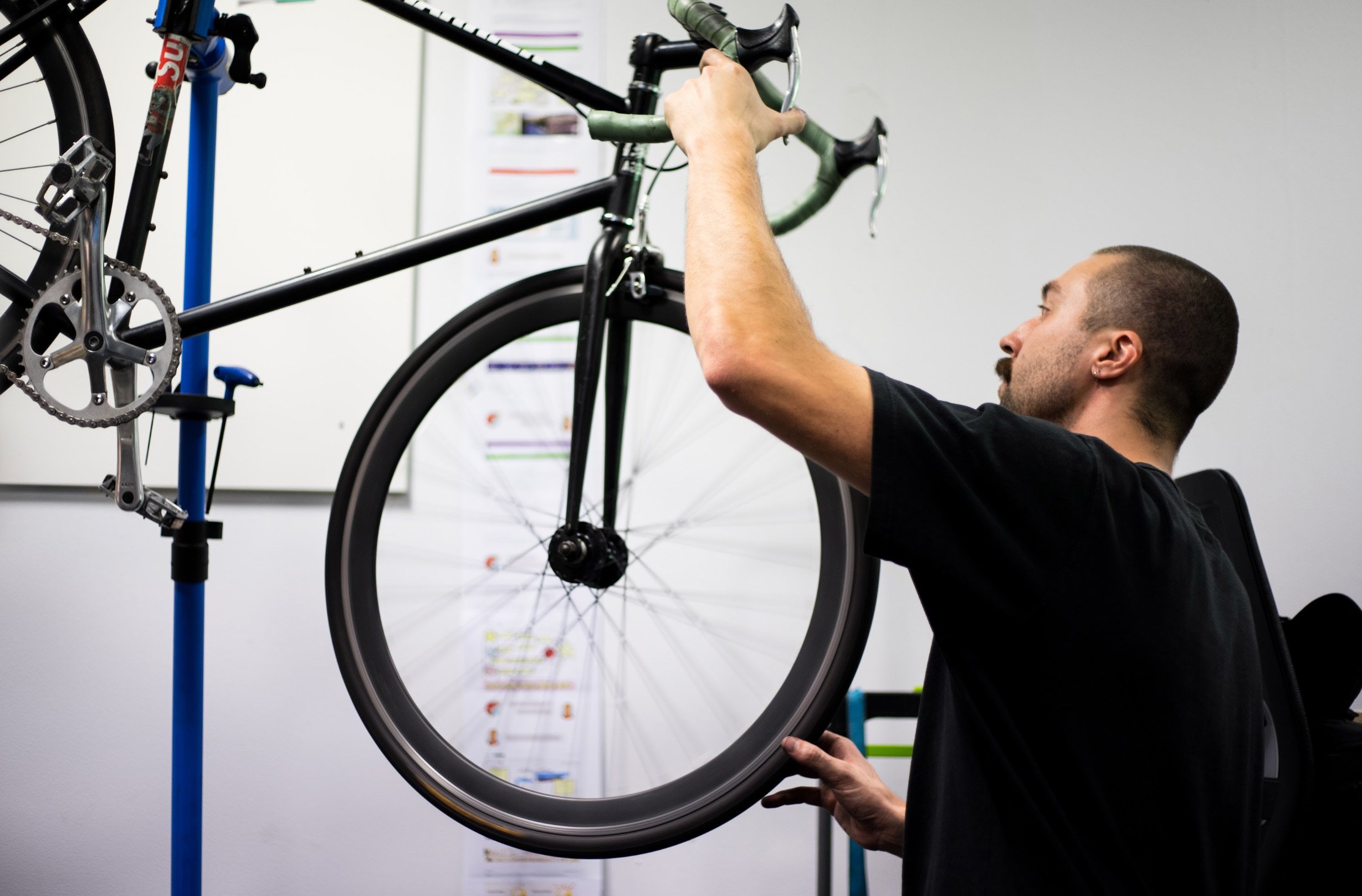 A man working on a bicycle mounted on a repair stand in a garage or workshop.