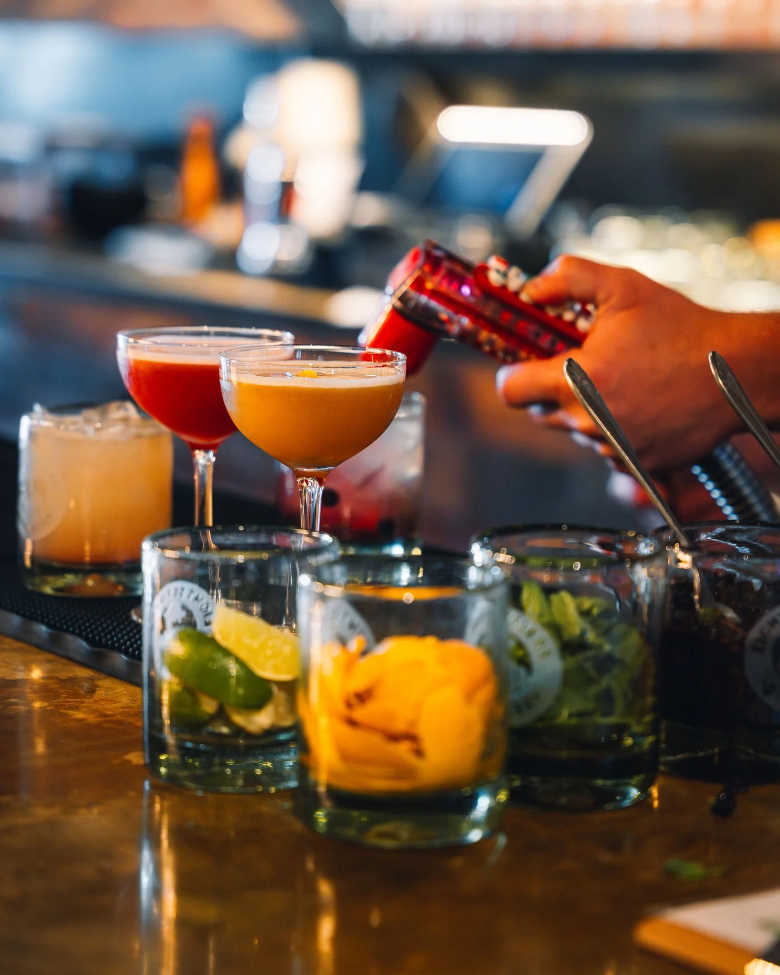 A bartender preparing colorful cocktails at a bar with various garnished glasses on the counter.