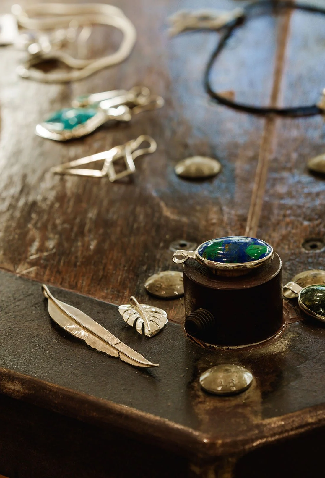 Close-up of assorted jewelry pieces, including a feather pendant, a leaf-shaped pendant, and a set of rings, displayed on a wooden surface.
