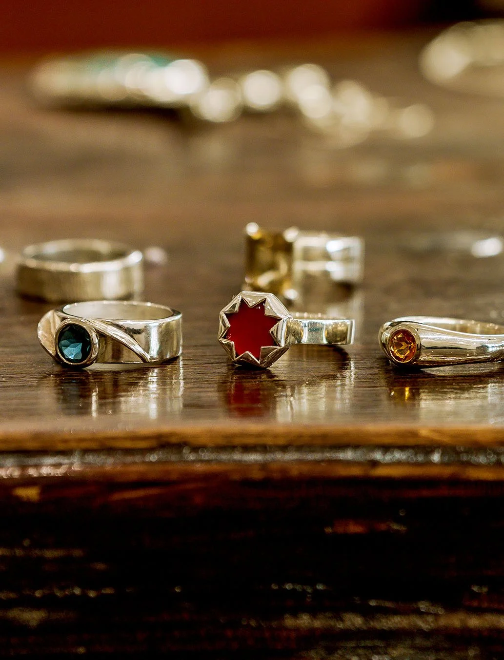 Various silver rings with colorful gemstones placed on a wooden surface.