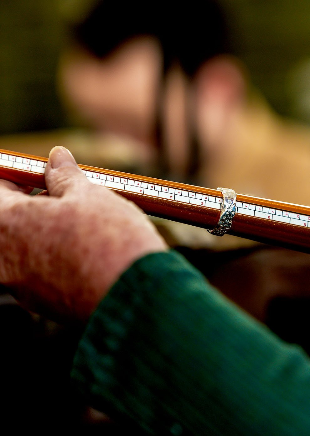 Close-up of a hand holding a traditional Chinese ruler, with a blurred figure in the background.