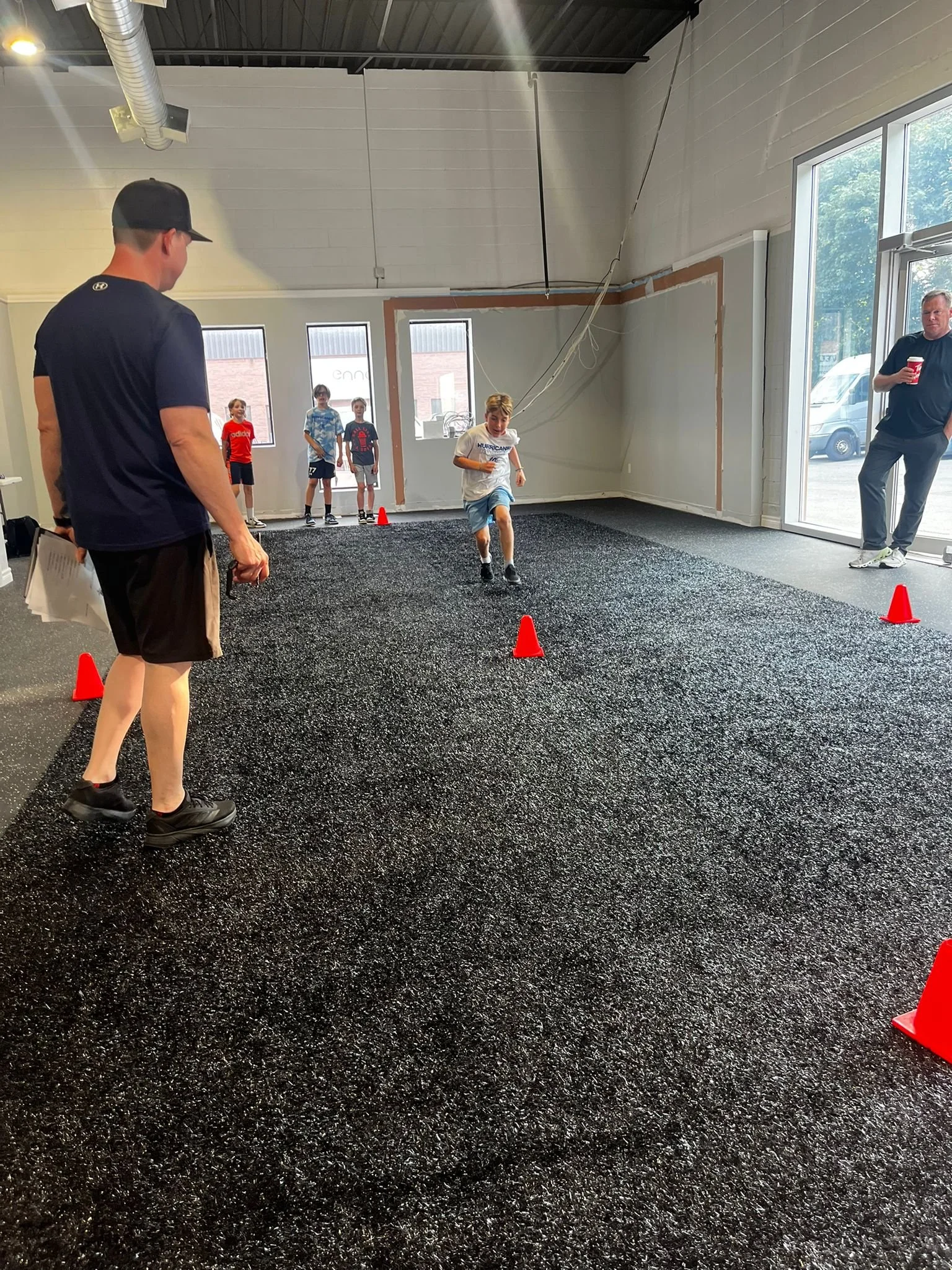 Children participating in an indoor running race, with orange cones marking the course, supervised by adults.
