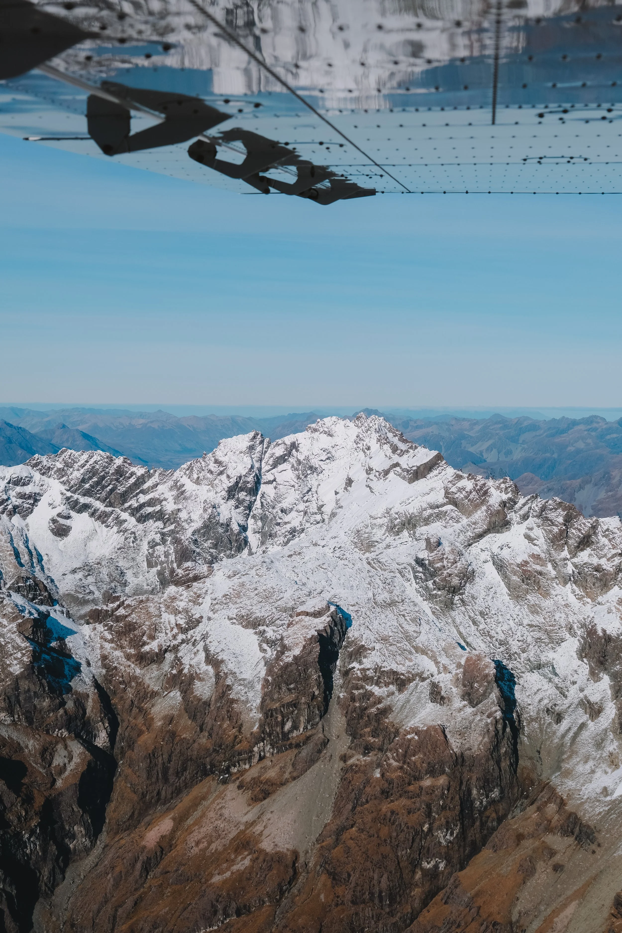 Aerial view of snow-capped mountain peaks taken from an aircraft with visible solar panels on the wing.