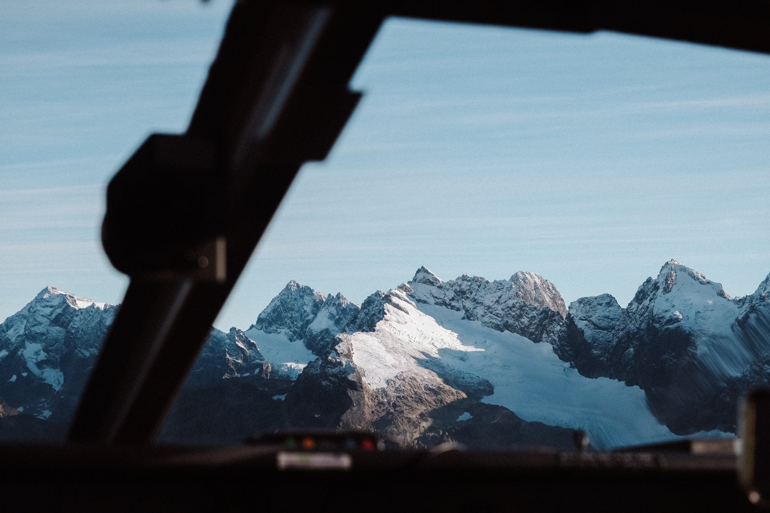 Snow-covered mountain peaks seen through the cockpit window of an airplane.