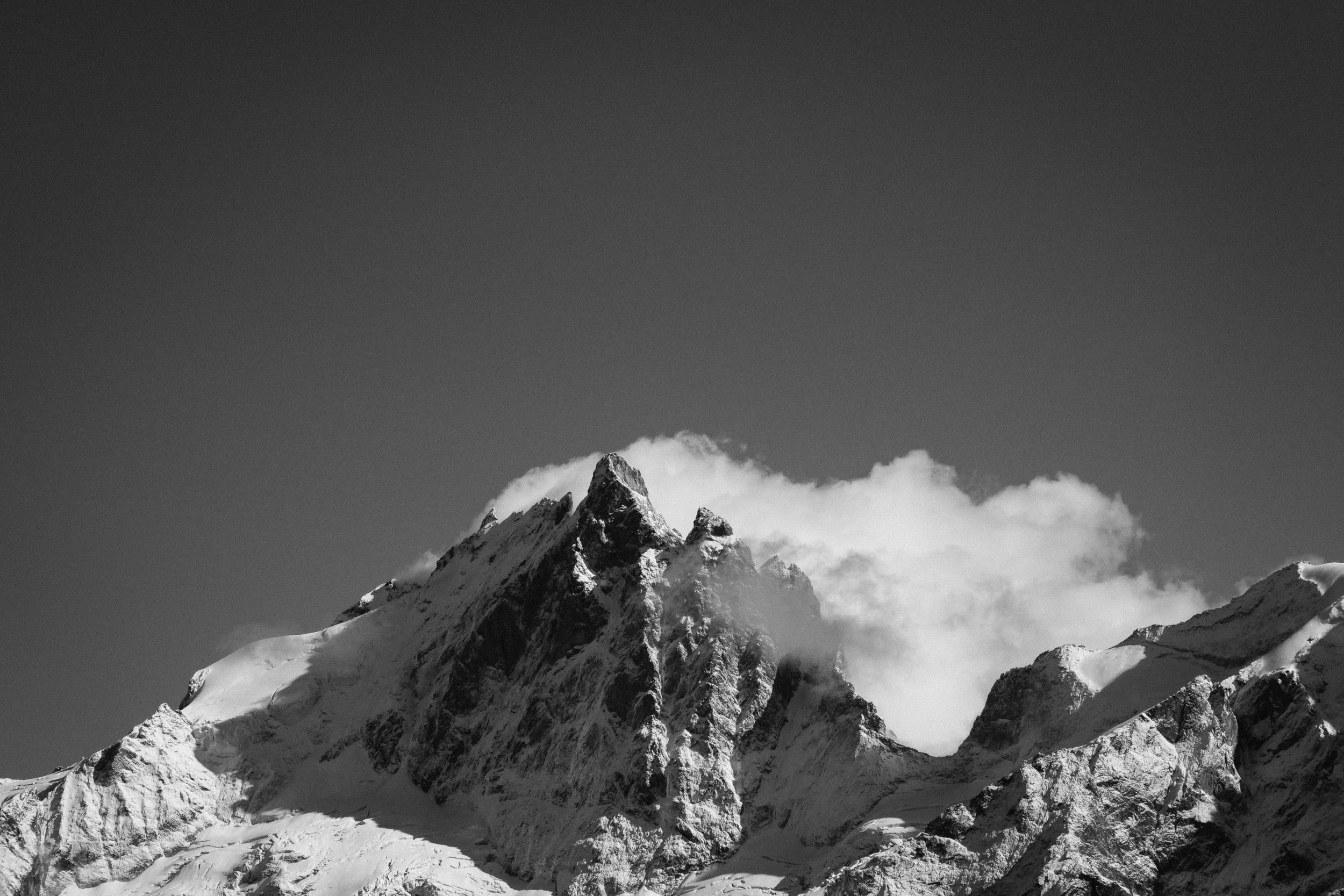 Black and white photograph of a snow-covered mountain peak with clouds around it.