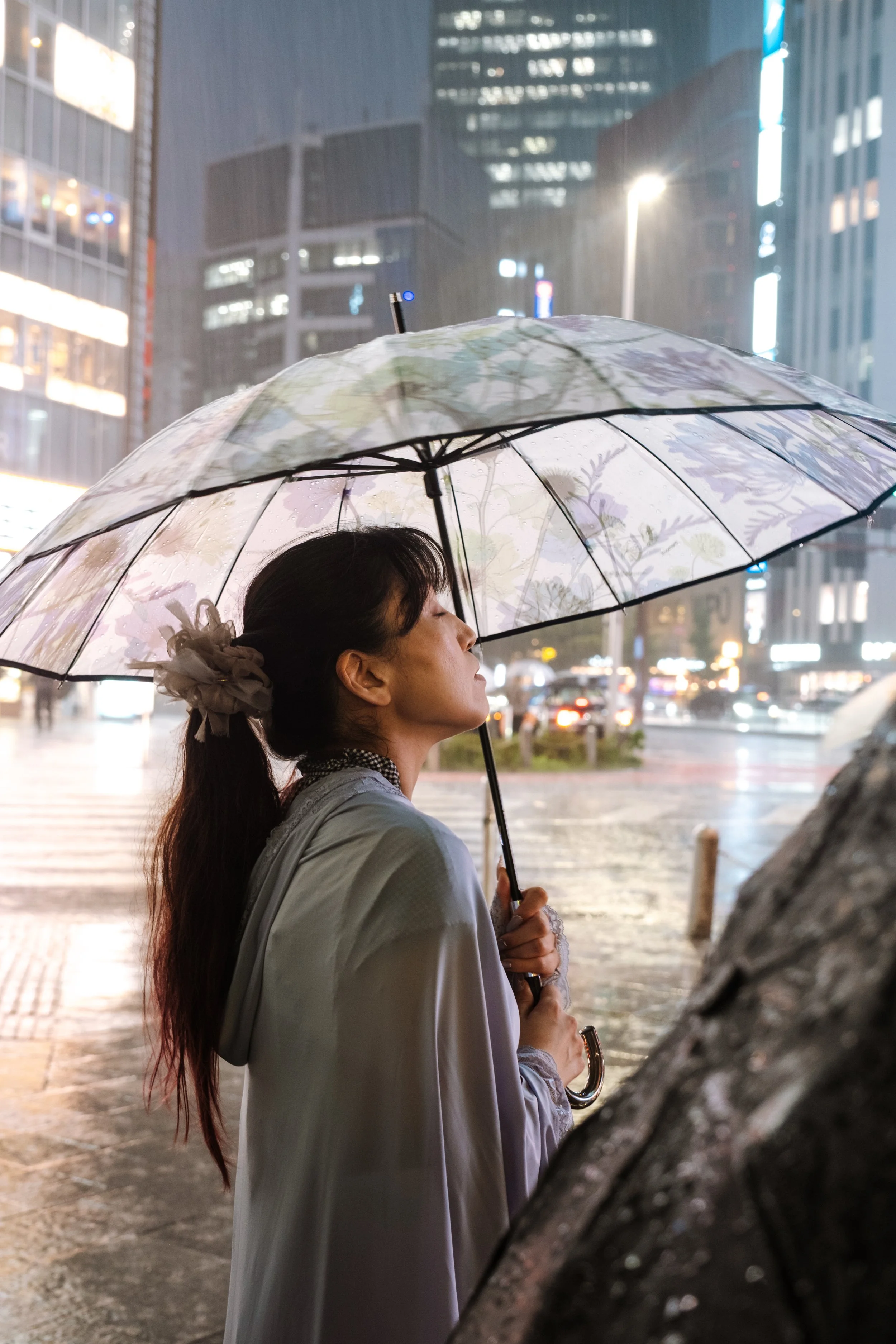 A woman standing in the rain holding an umbrella with her eyes closed and face tilted upwards