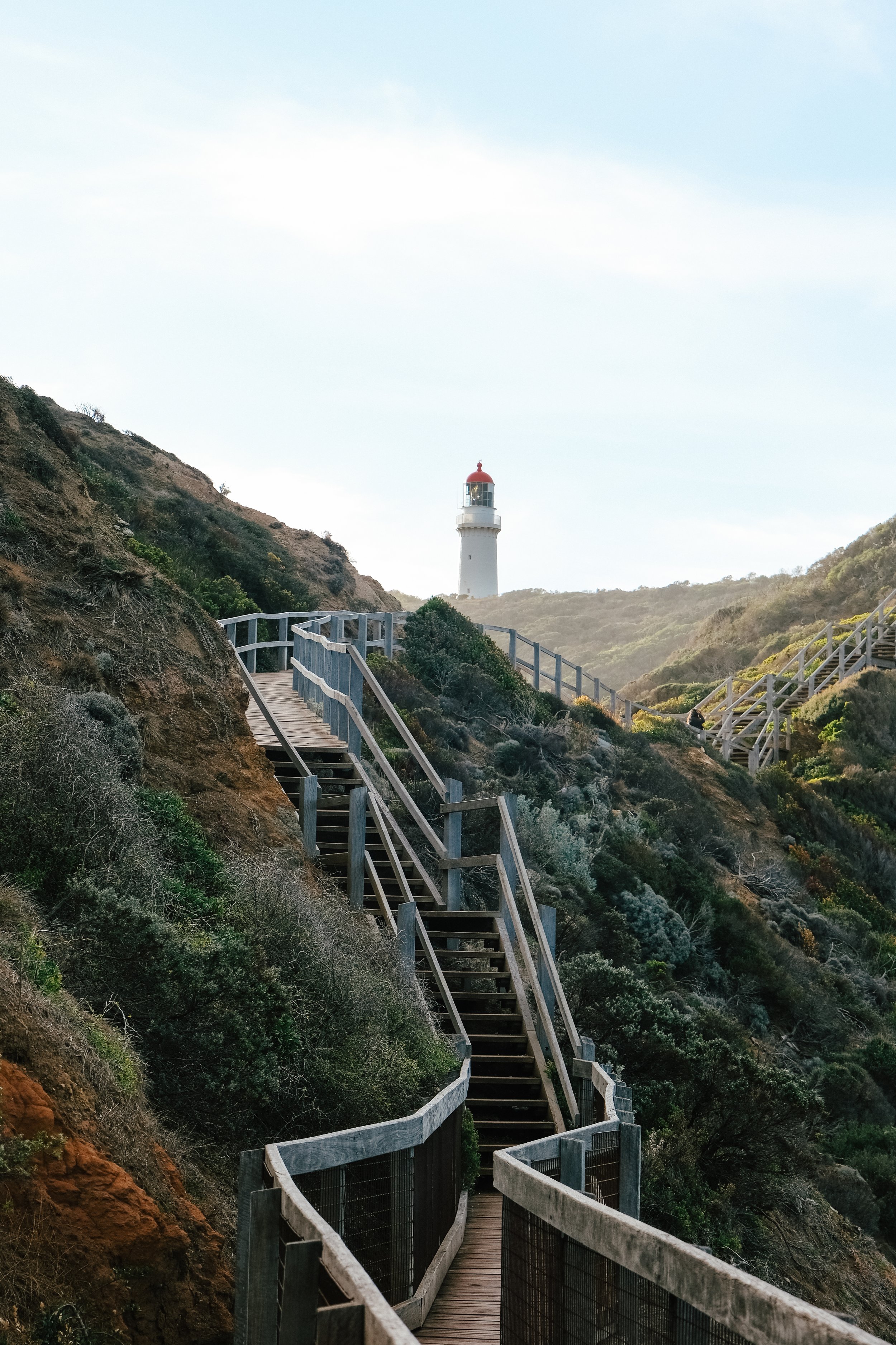 A winding wooden staircase on a hillside leading up to a lighthouse in the distance.