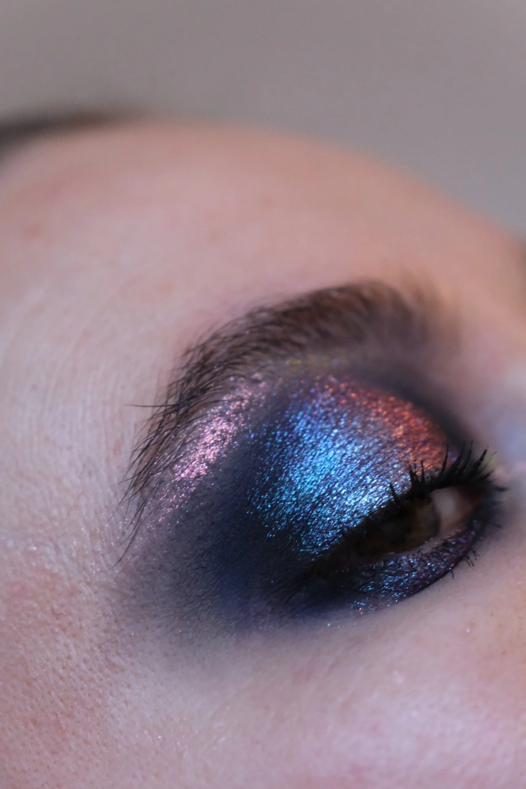 Close-up of a person's eye with colorful, glittery eyeshadow in shades of pink, purple, and blue.