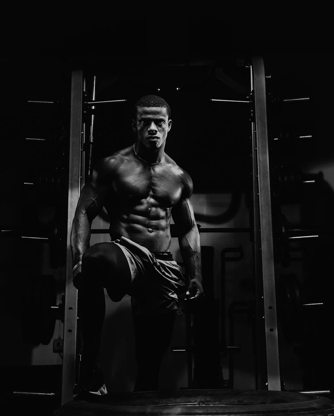 A muscular man with defined abs posing in a gym, black and white photo.