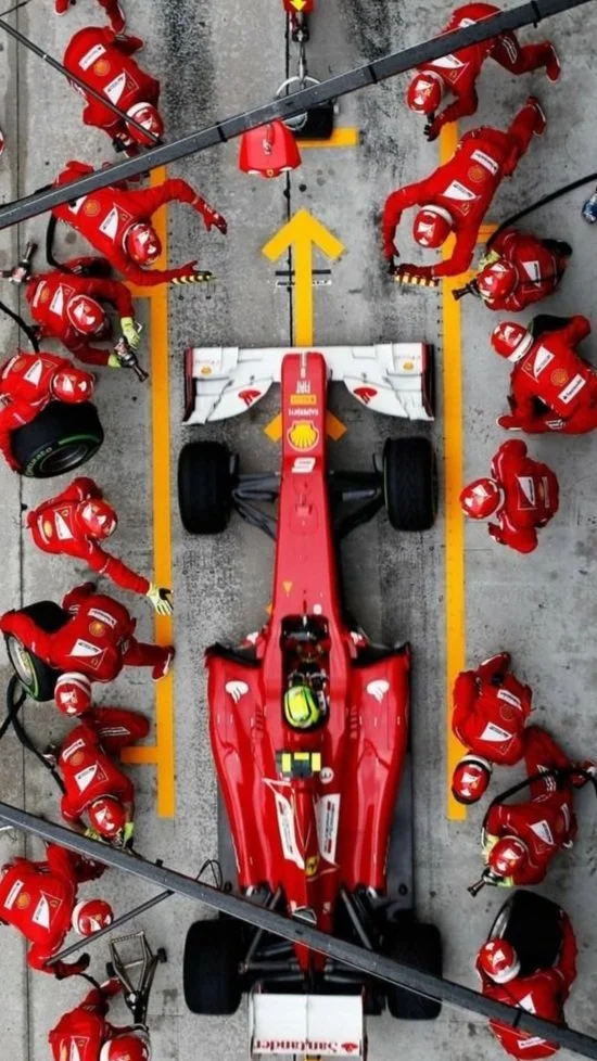 Top-down view of a red Formula 1 race car in the pit stop with a team of mechanics surrounding it, working on the car.