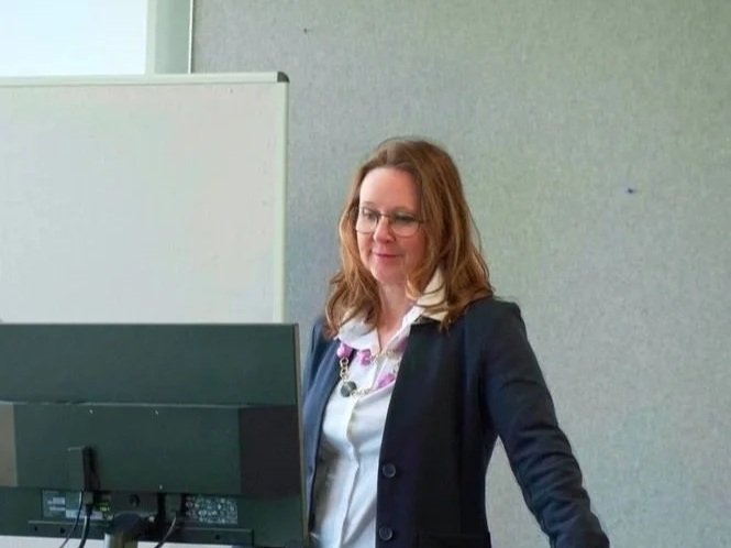 Woman with glasses and brown hair working at a computer in an office setting.