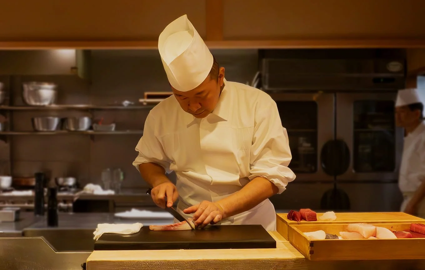 寿司職人が包丁で魚をさばいている。