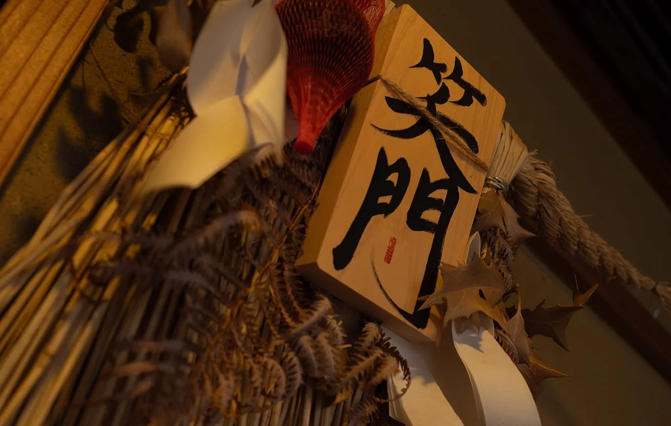 神社の入口に掛けられたしめ縄飾りと木製の札。札には大きな黒色の文字で「姿門」と書かれている。
