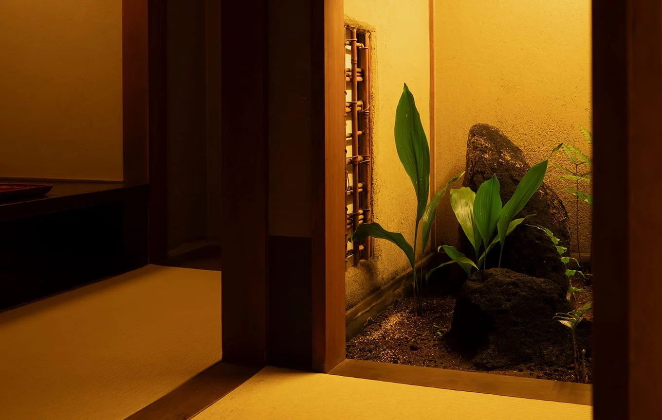 和室の一部と、その奥にある小さな庭。庭には緑の植物と岩が置かれている。