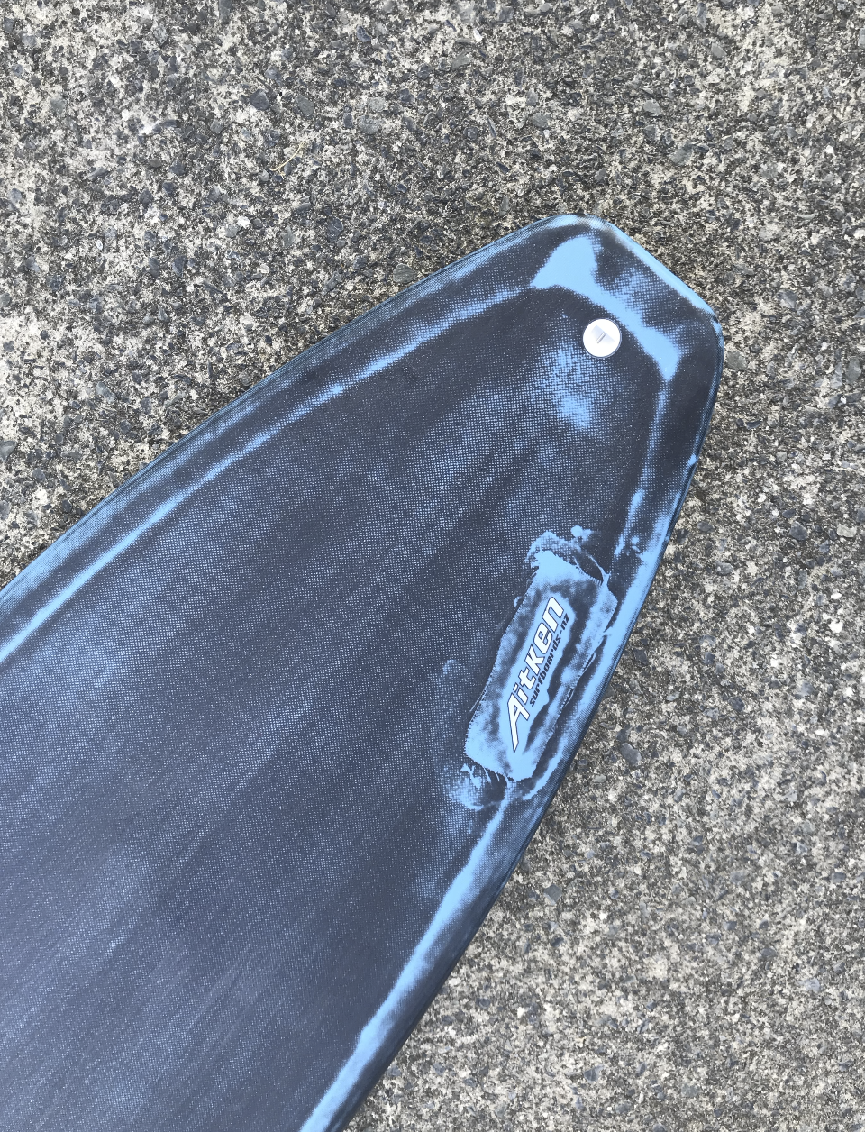 A blue and black trampoline with a brand logo on the ground. Aitken Surfboards