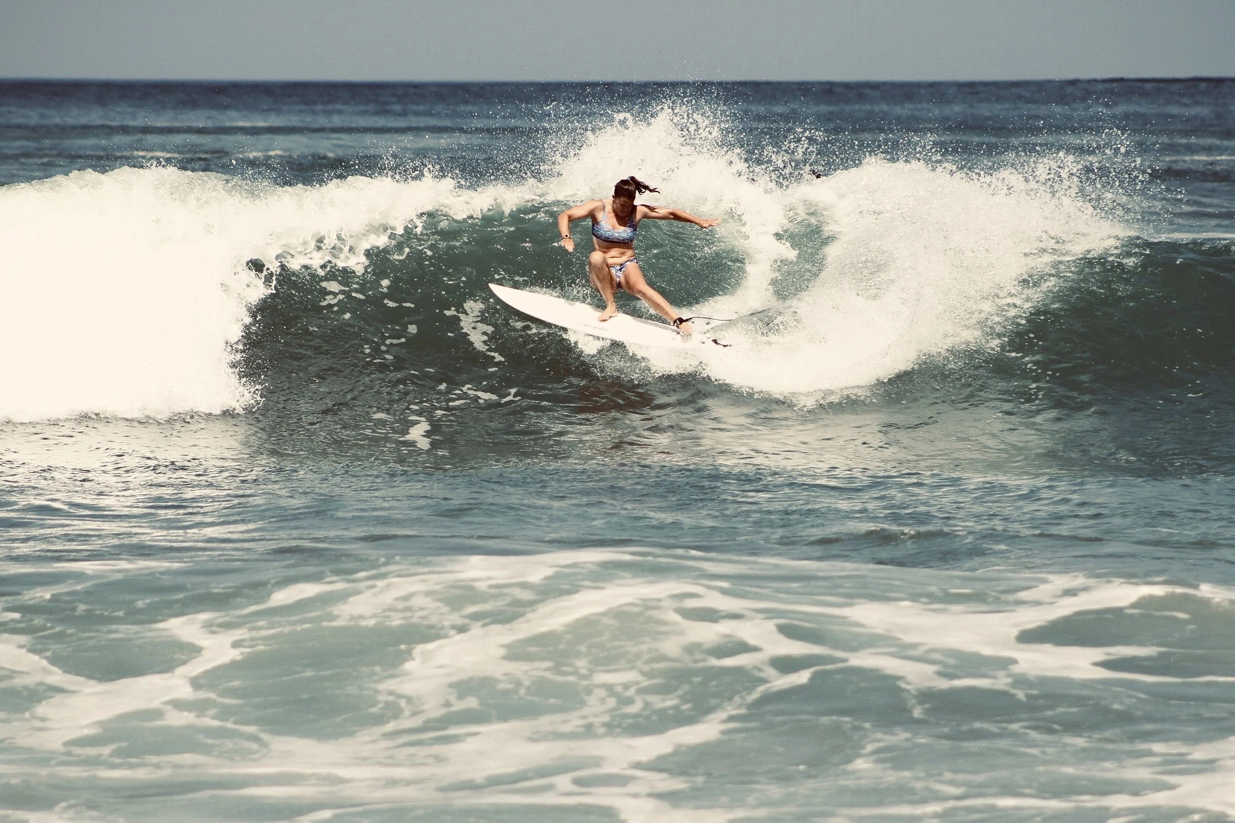 A woman surfing on a wave in the ocean. Aitken Surfboards