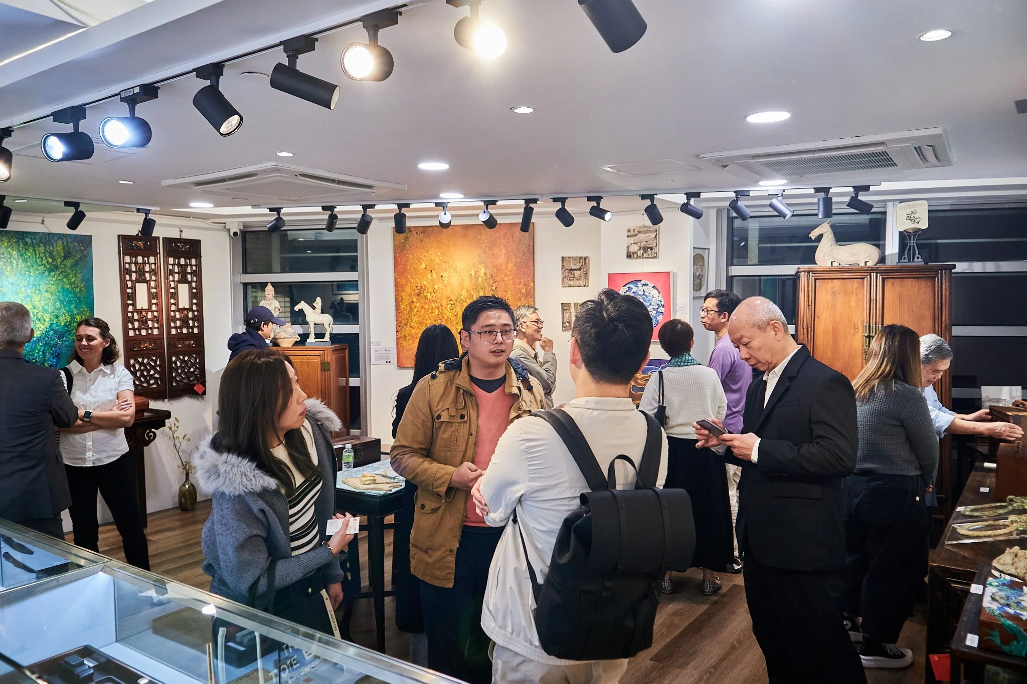 People attending an art gallery or exhibition, engaging in conversations and viewing artworks and sculptures.