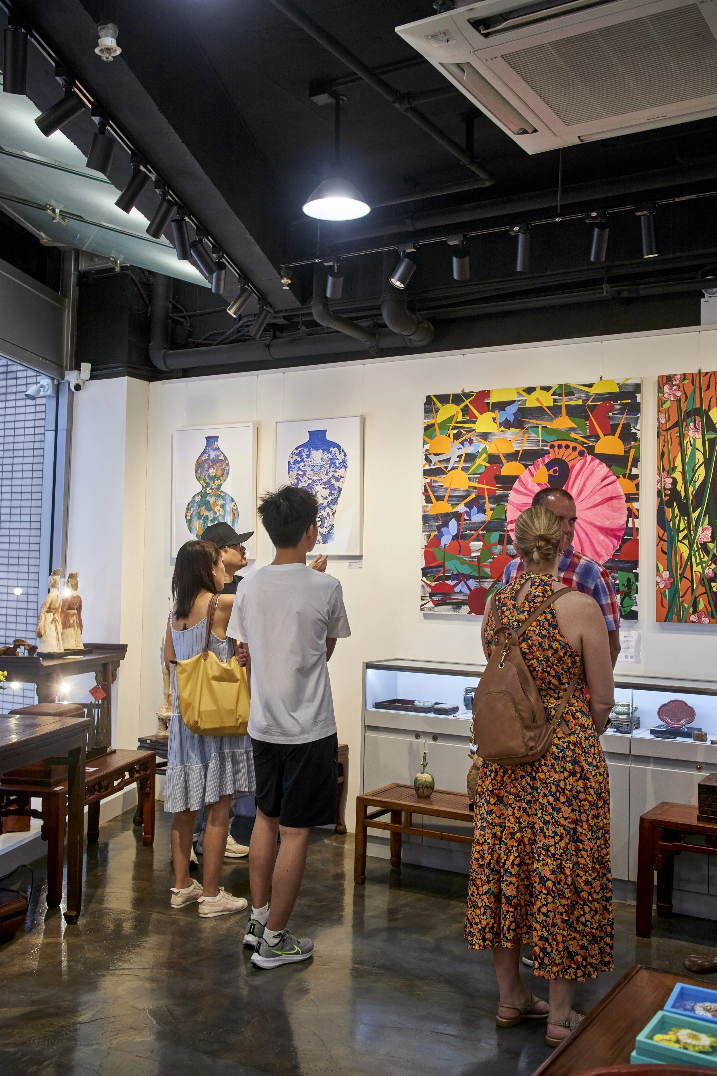 People viewing artwork in an art gallery, with colorful paintings and ceramics displayed on white walls.