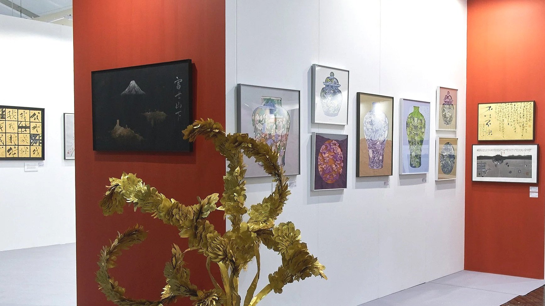 Art Central 2025: Art gallery interior with various framed artworks on white and red walls, and a gold-colored sculpture resembling a twisted branch or vine in the foreground.