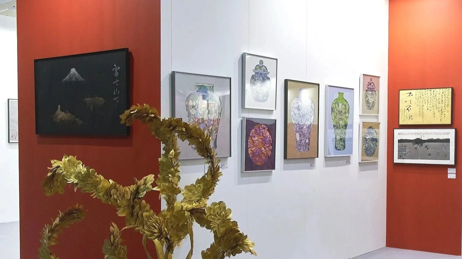 Art Central 2025: Art gallery with framed artwork on white and red walls, including vases and calligraphy, and a decorative gold-colored sculpture in the foreground.
