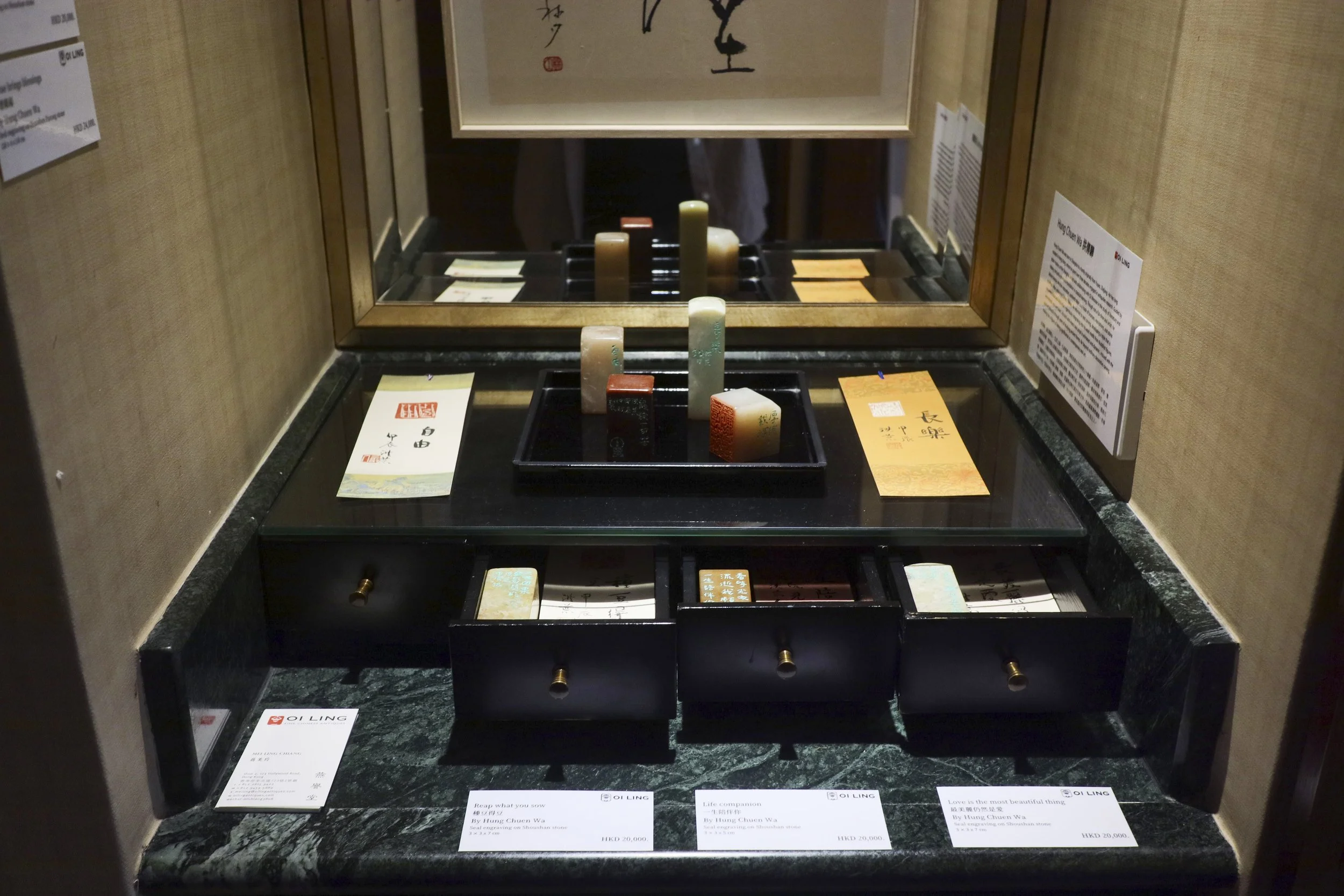 Whatz Art Fair 2025: Display of various traditional Chinese seals and stamps on a black table, with informational cards and a mirror reflecting the items.
