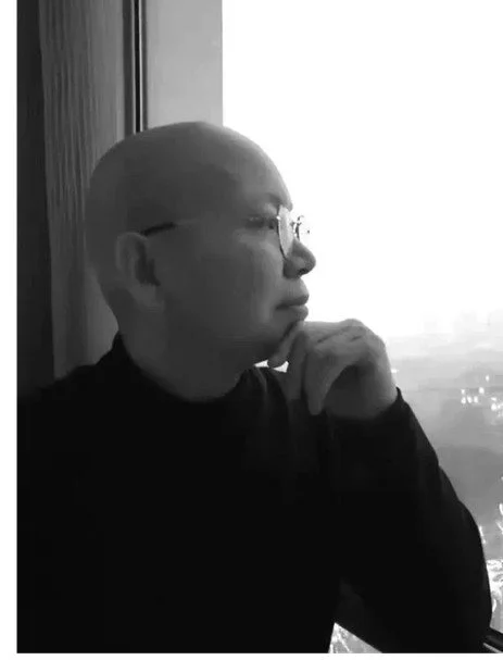 Tian Yanhua 田言華：A bald person wearing glasses sitting by a window, looking outside thoughtfully.