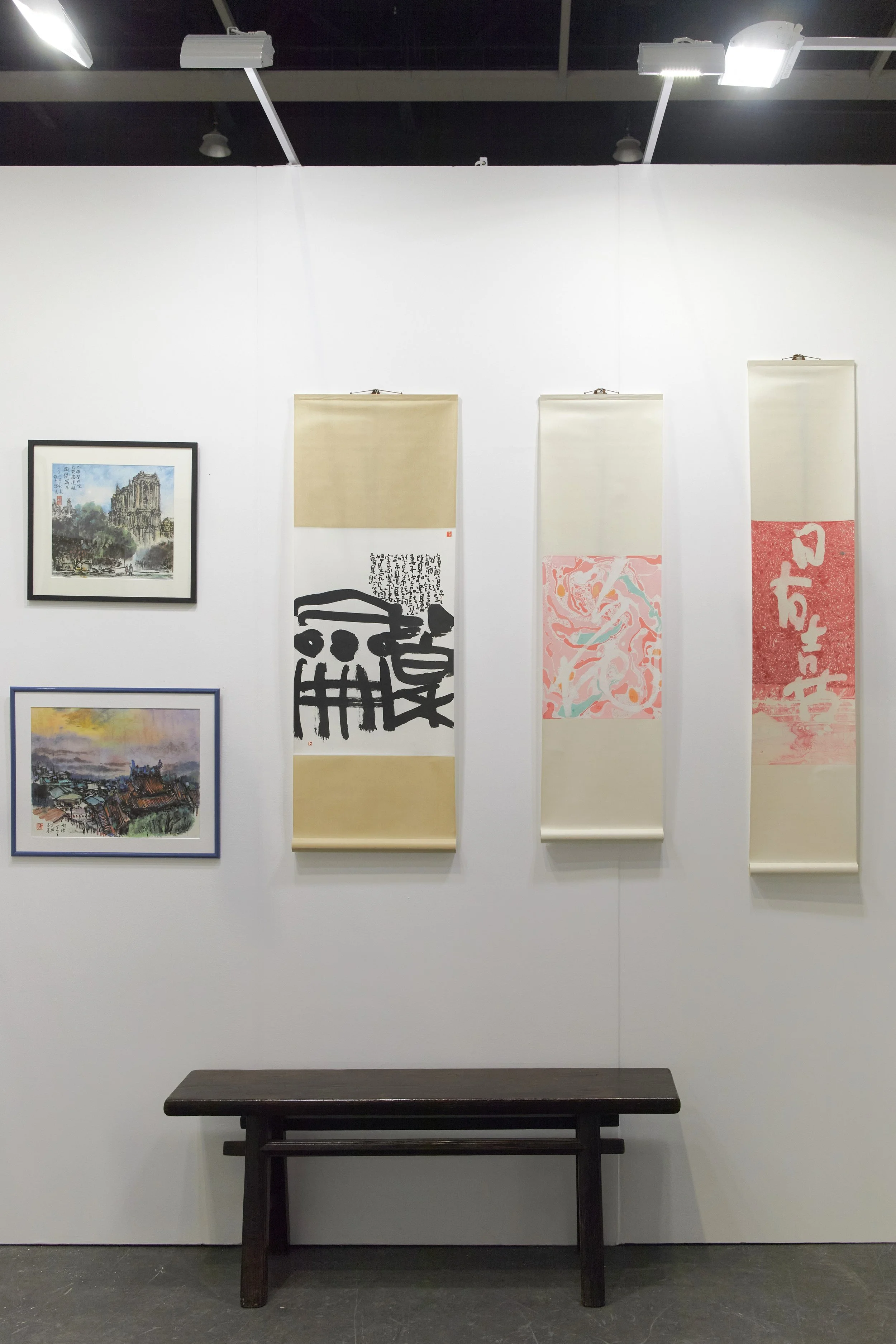 Affordable Art Fair 2025: Gallery wall with two framed landscape paintings, three Asian calligraphy scrolls, and a bench below.
