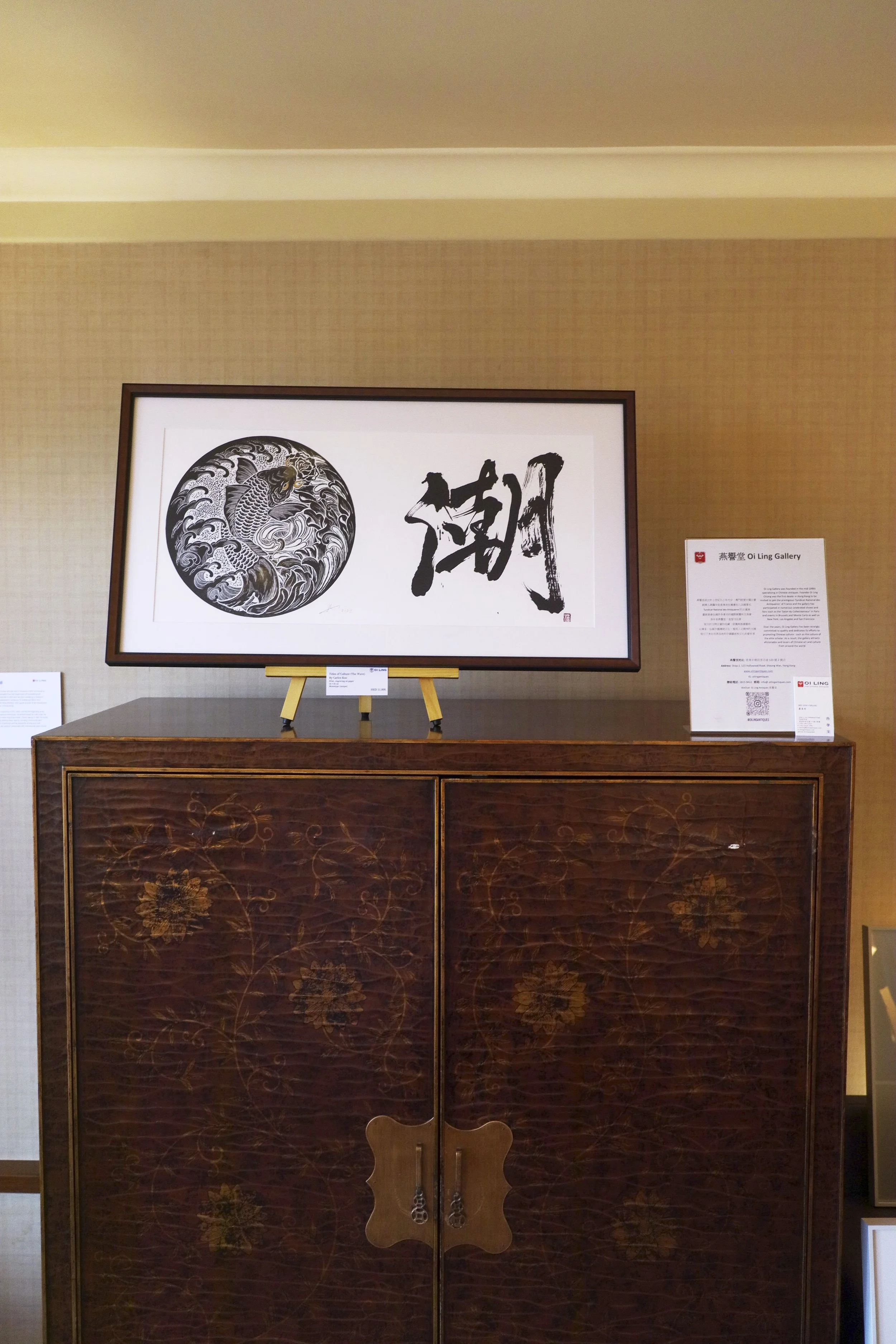 Whatz Art Fair 2025: Framed Asian art piece featuring a koi fish illustration and Chinese calligraphy, displayed on a wooden cabinet in an art gallery.