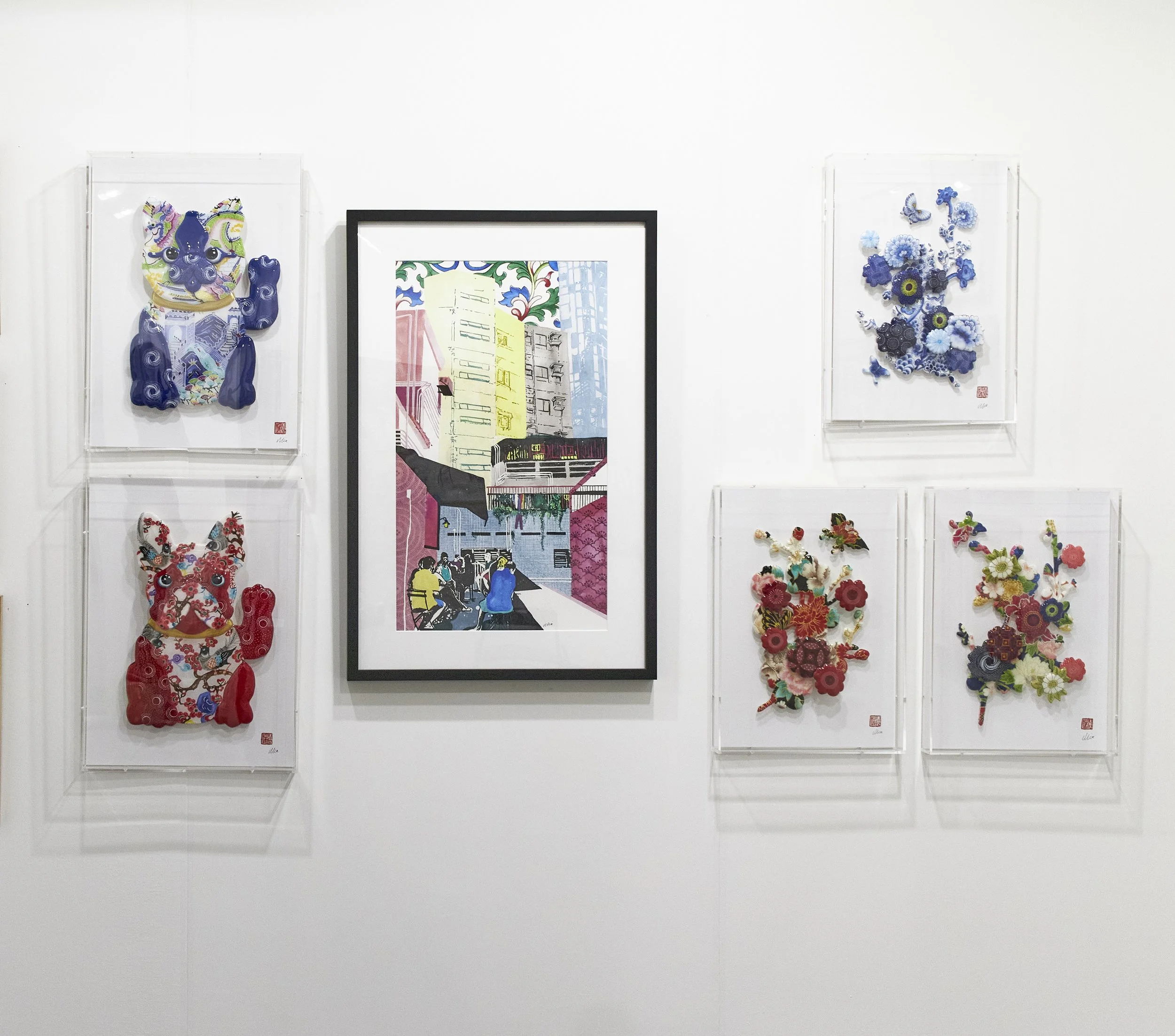 An art gallery wall displaying six framed artworks. The two send and right frames feature colorful, textured sculptures of dog figures, while the three frames in the middle display floral and butterfly motifs. The center frame is a colorful city stre