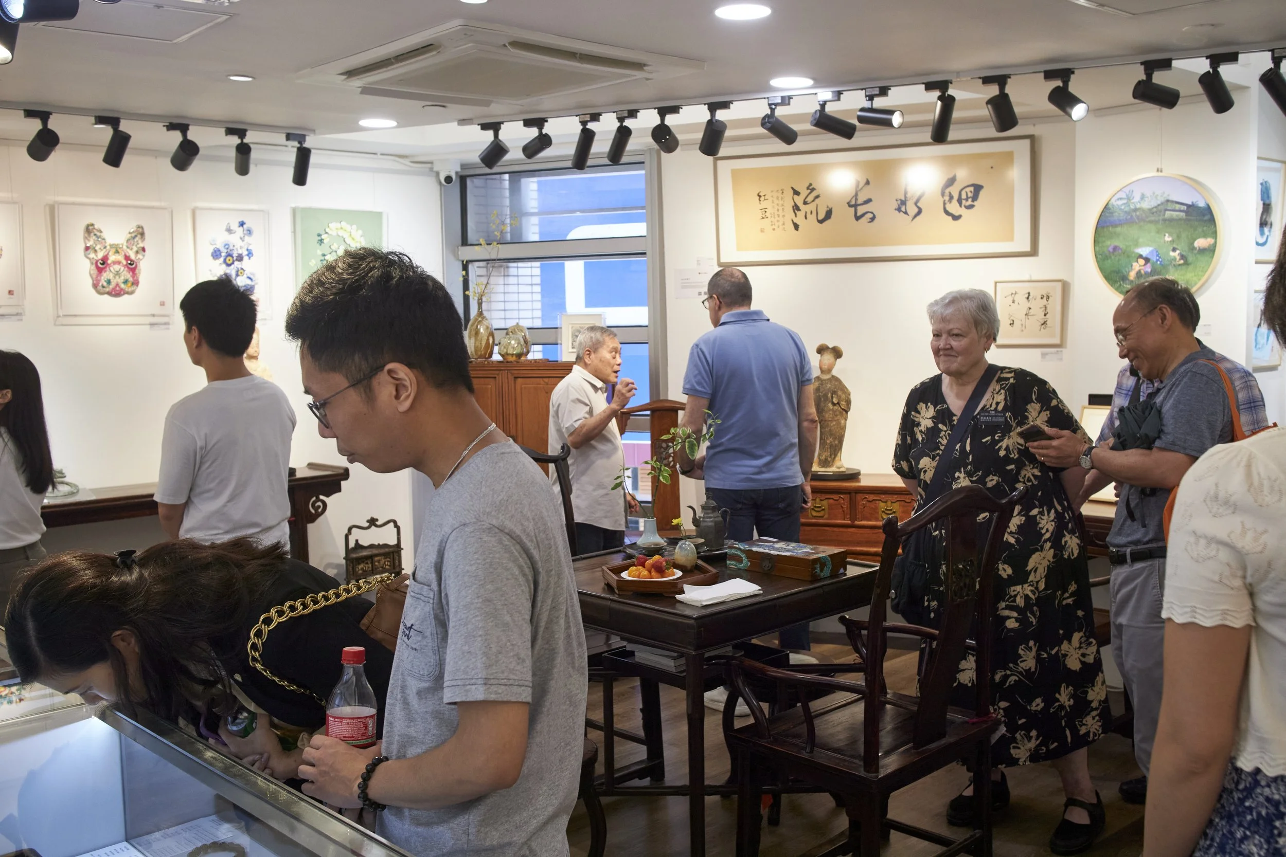 People inside an art gallery, some looking at artwork on the walls, others browsing displays and talking.