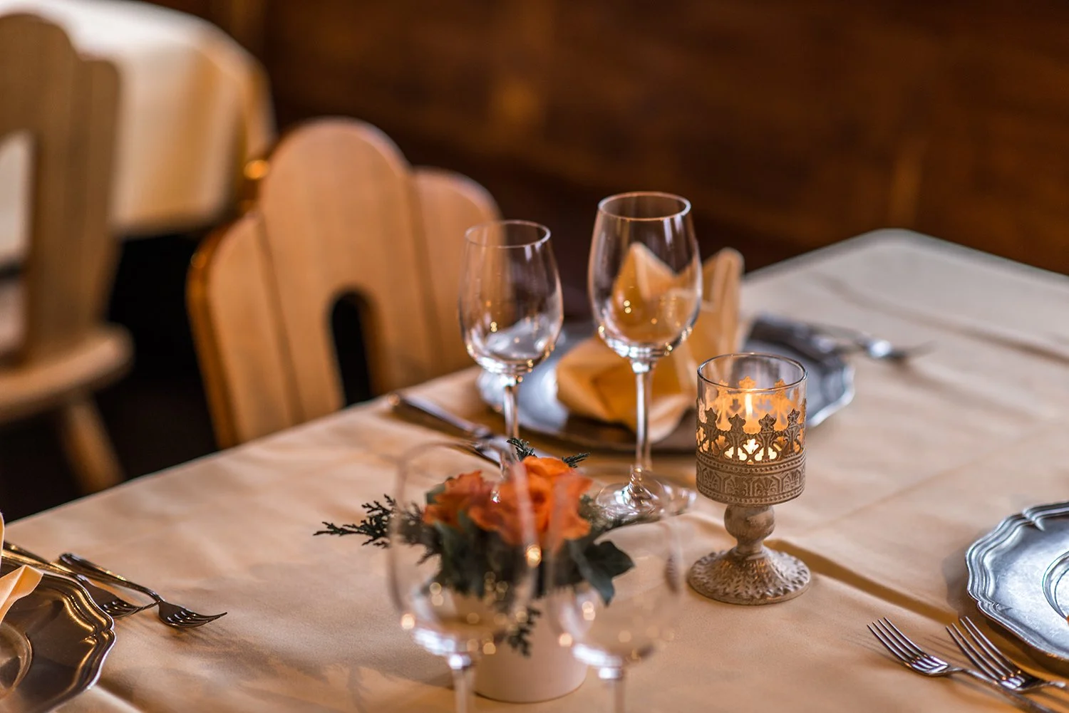 Eleganter gedeckter Tisch mit Weingläsern, einer Kerzenhalter, Besteck, Stoffservietten und Dekorationsblumen, bereit für eine Mahlzeit.