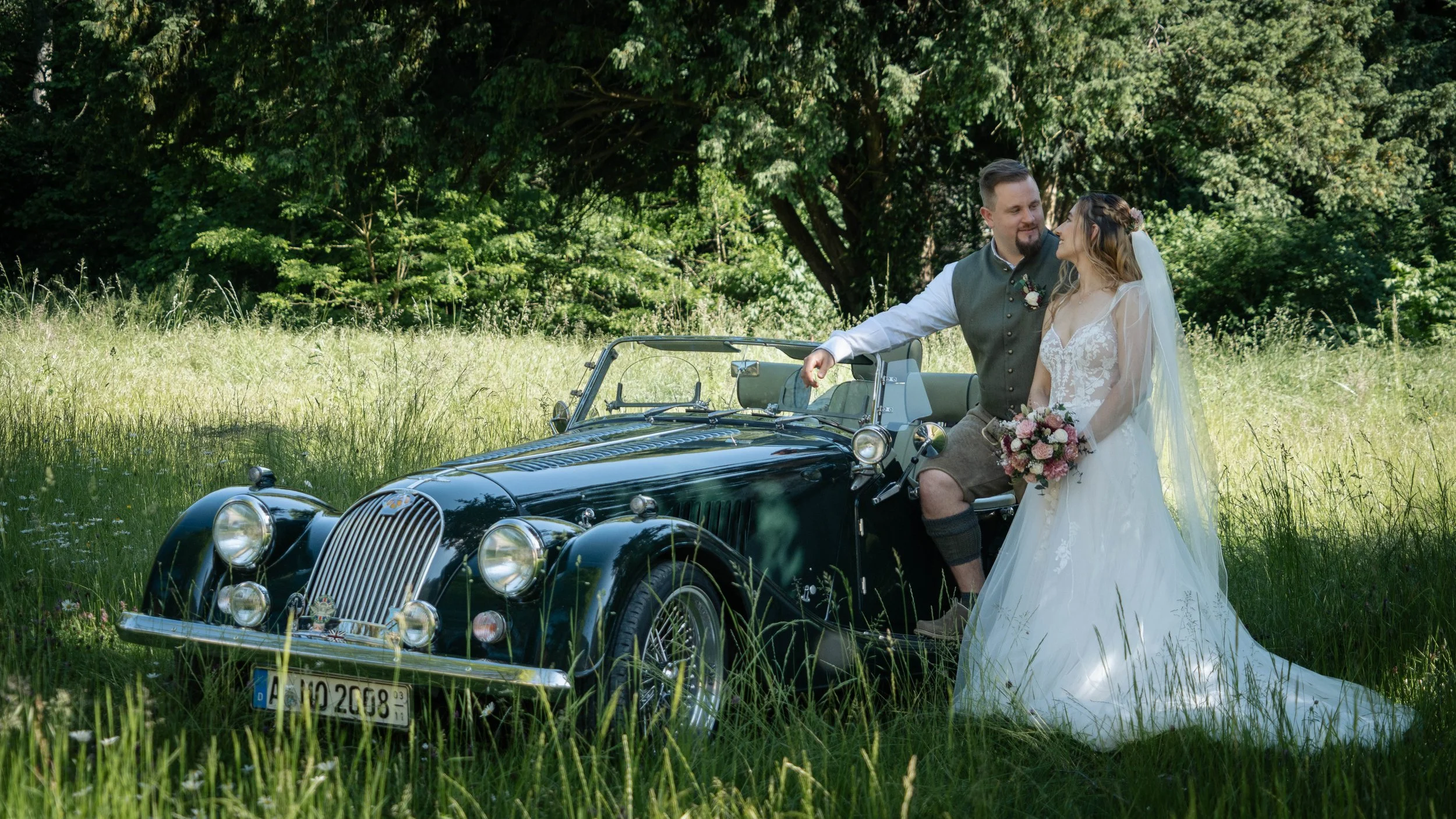 Brautpaar am grünen Morgan Roadster als Hochzeitsauto auf einer Wiese