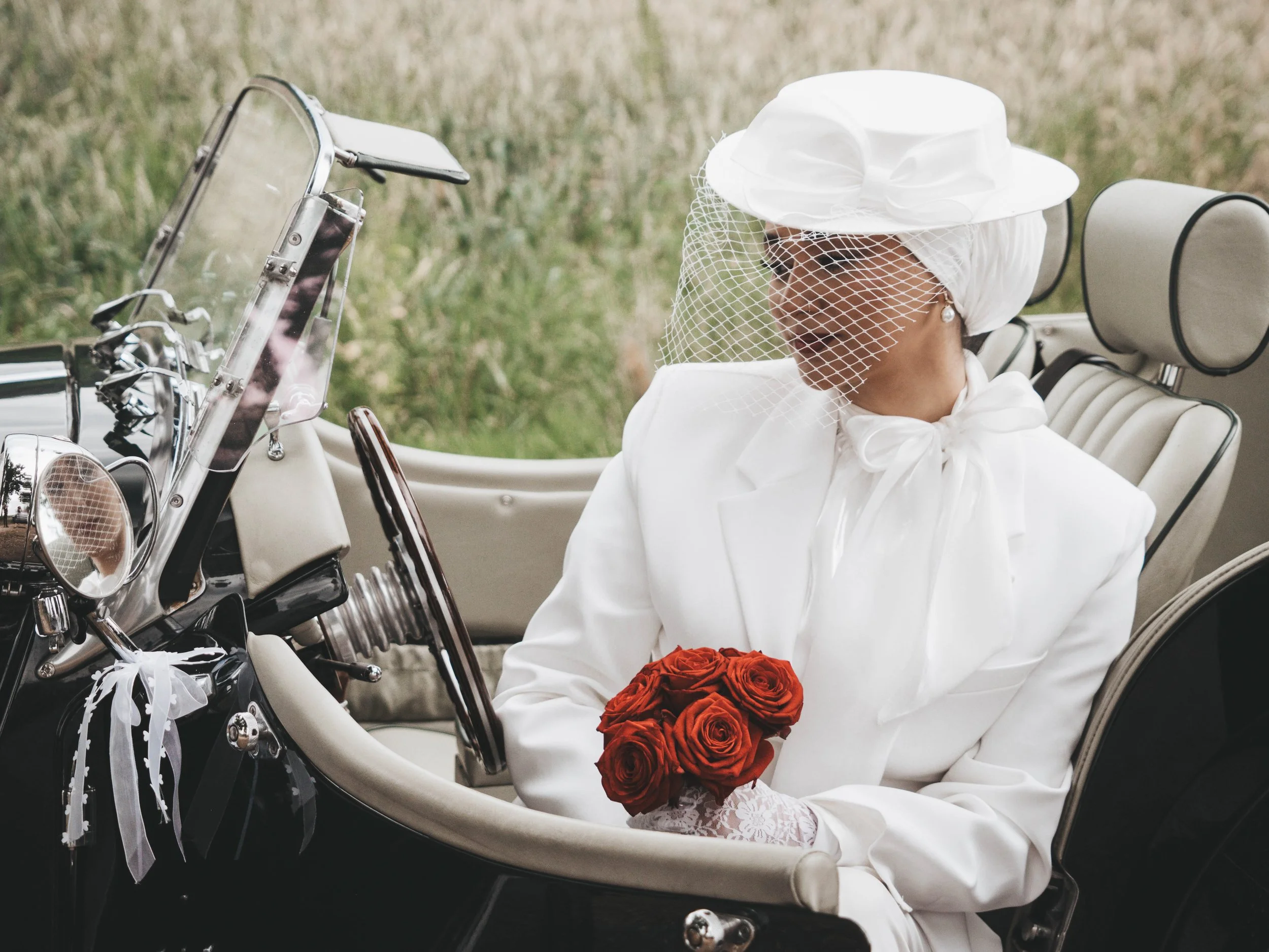 Braut mit Hut und rotem Brautstrauß im offenen Morgan Roadster