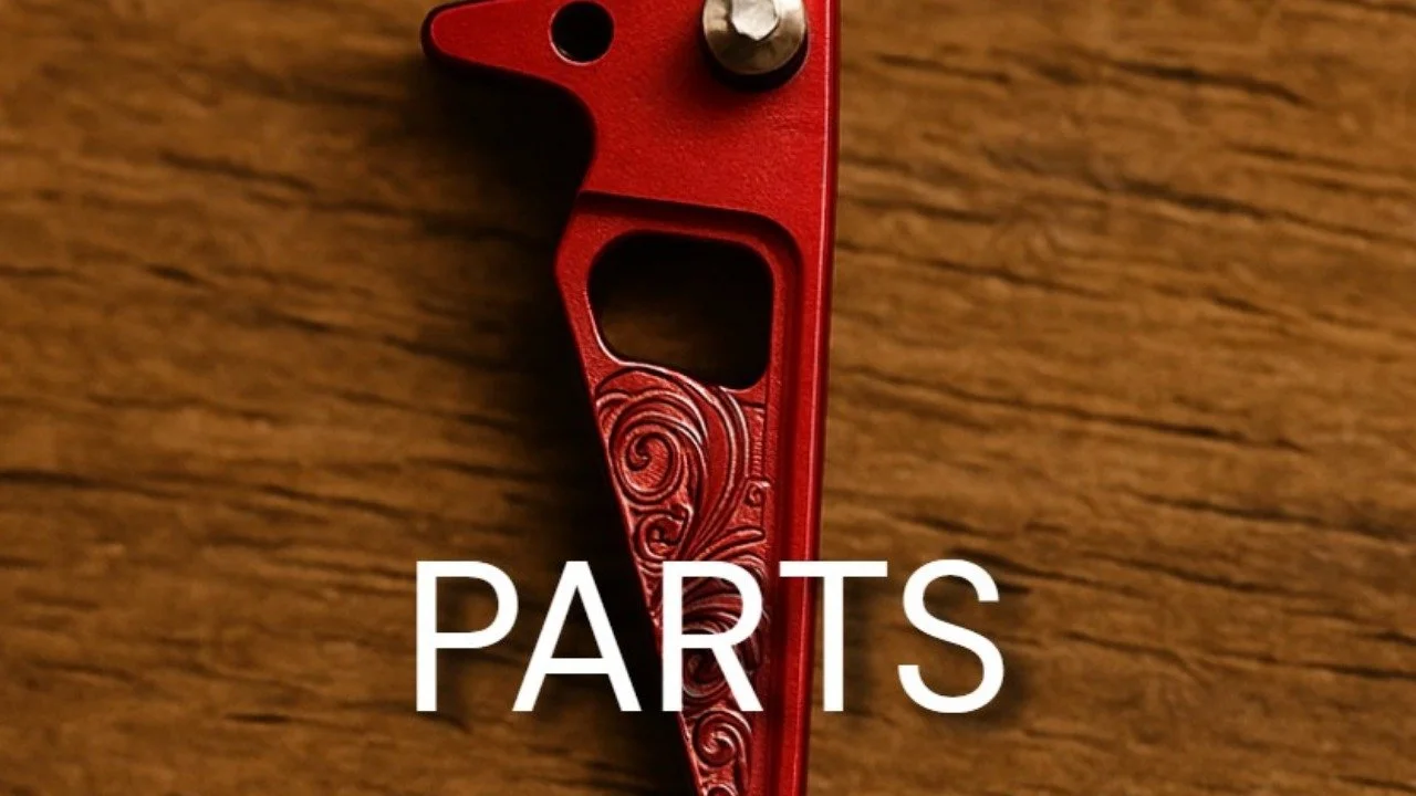 Close-up of a red metallic part with a decorative swirl design on a wooden surface, with the word 'PARTS' written across it.