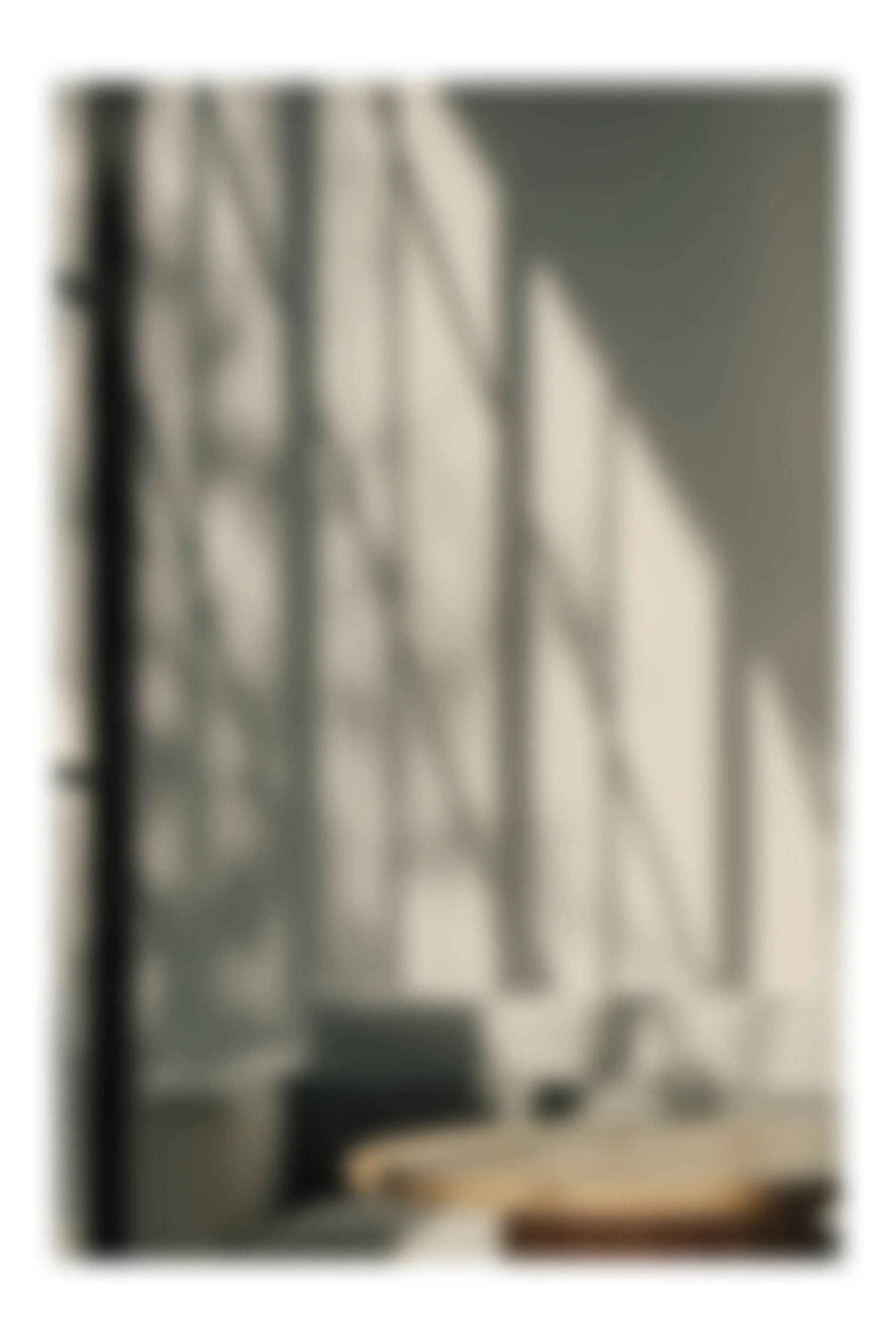 Sunlight casting geometric shadows on a wall behind a white sofa with dark pillows, near a round wooden table.