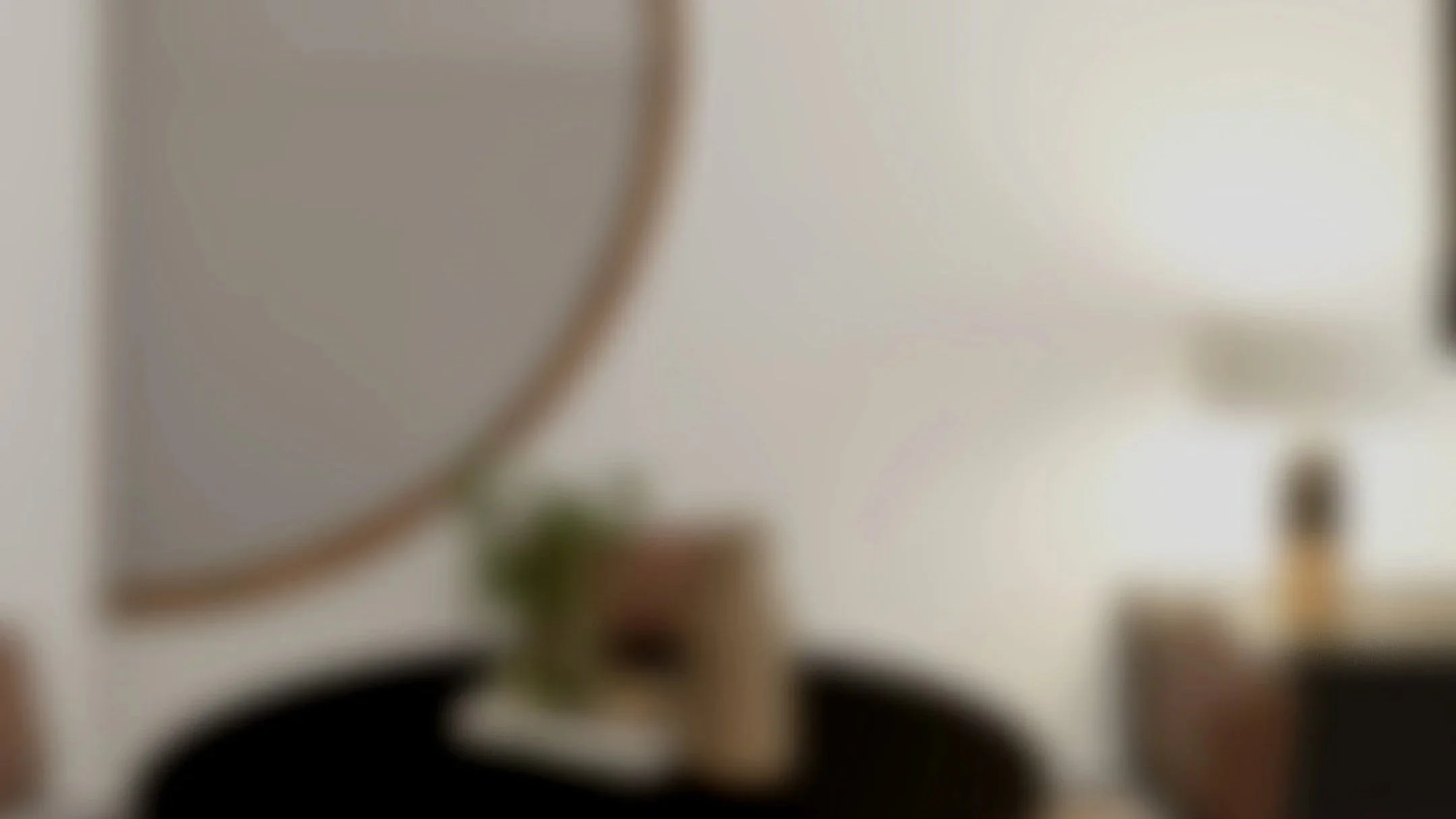 Minimalist living room with a black sofa, wooden coffee table, side table, and a decorative vase with dried plants, viewed through an arched doorway.