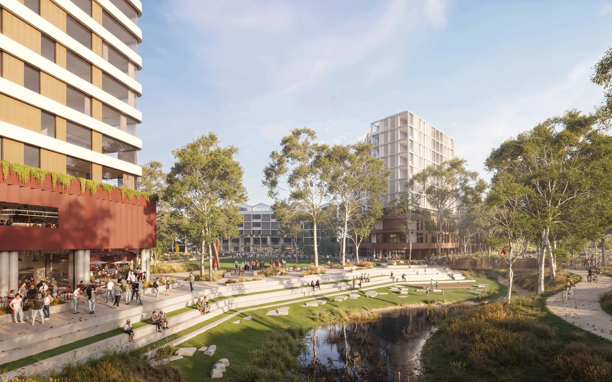 An outdoor urban park with tiered seating, a small body of water, trees, and modern multi-story buildings with glass windows and balconies in the background. People are walking, sitting, and cycling.