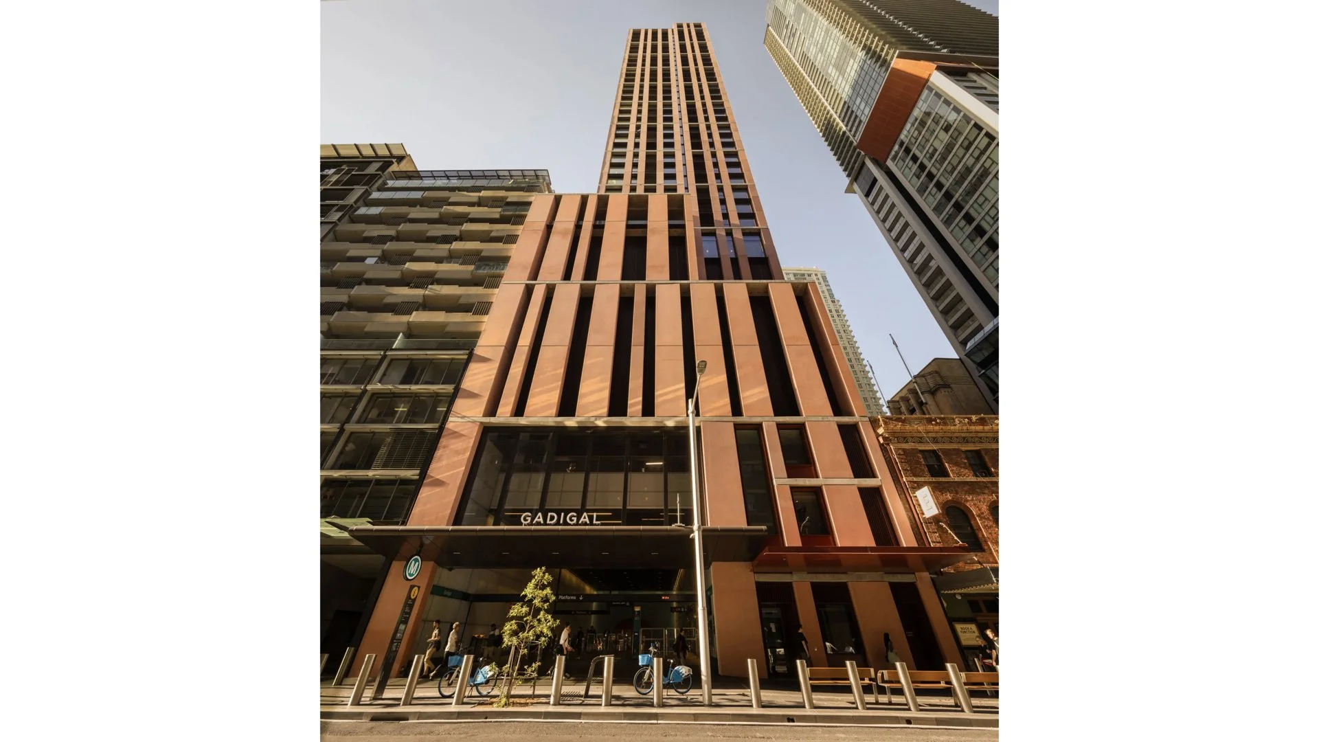 Tall modern skyscraper with a reddish-brown facade and large windows, located on a city street with pedestrians and bicycles in front.
