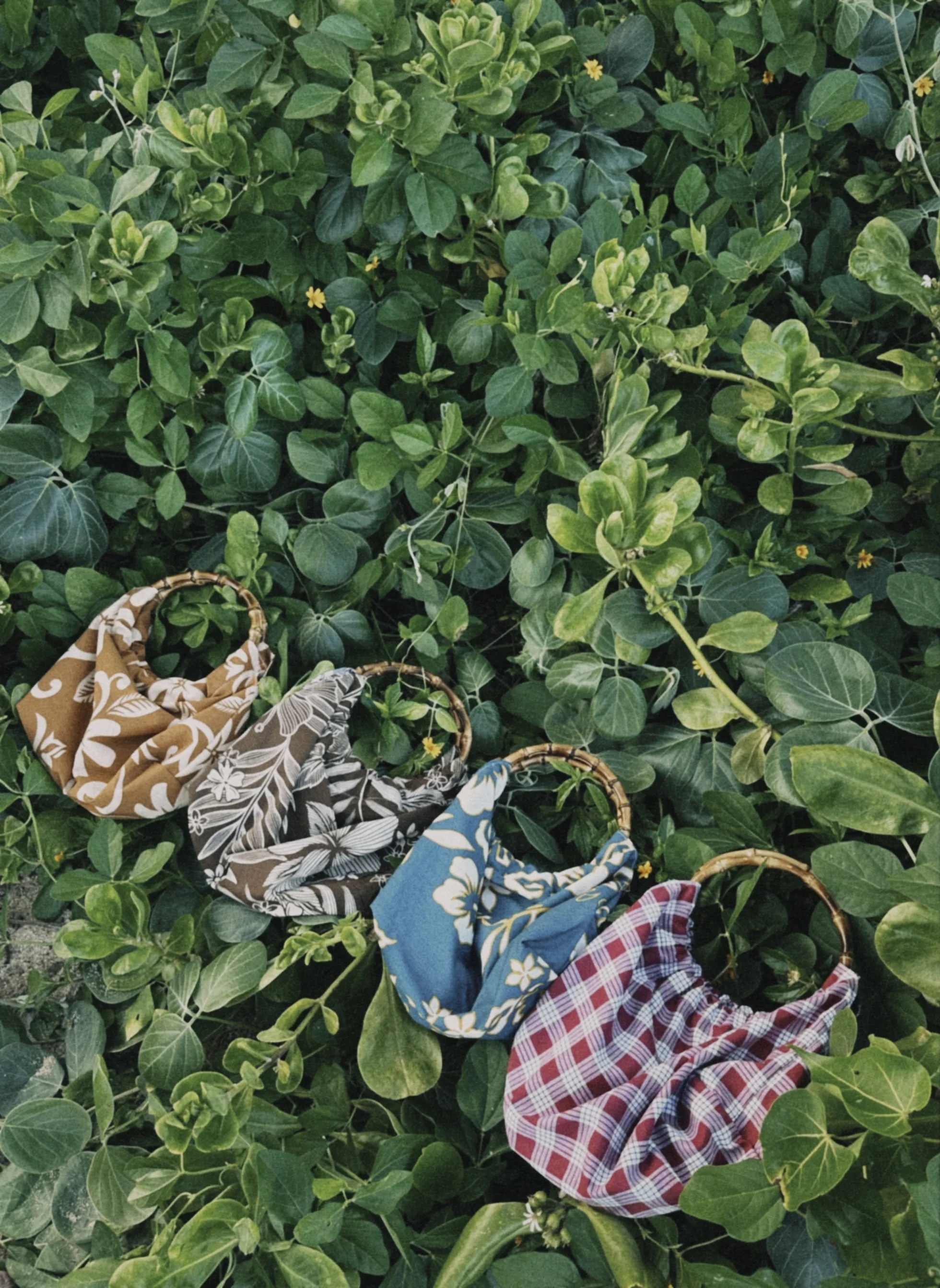 Four small bags with Polynesian prints laid on the grass