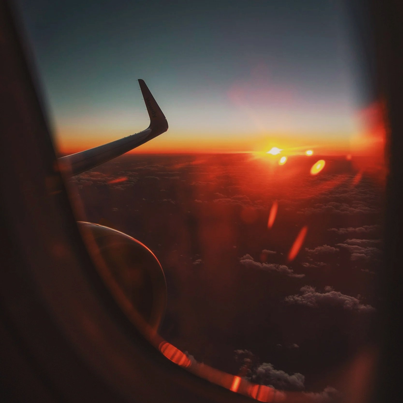 Sunset viewed from an airplane window above the clouds.