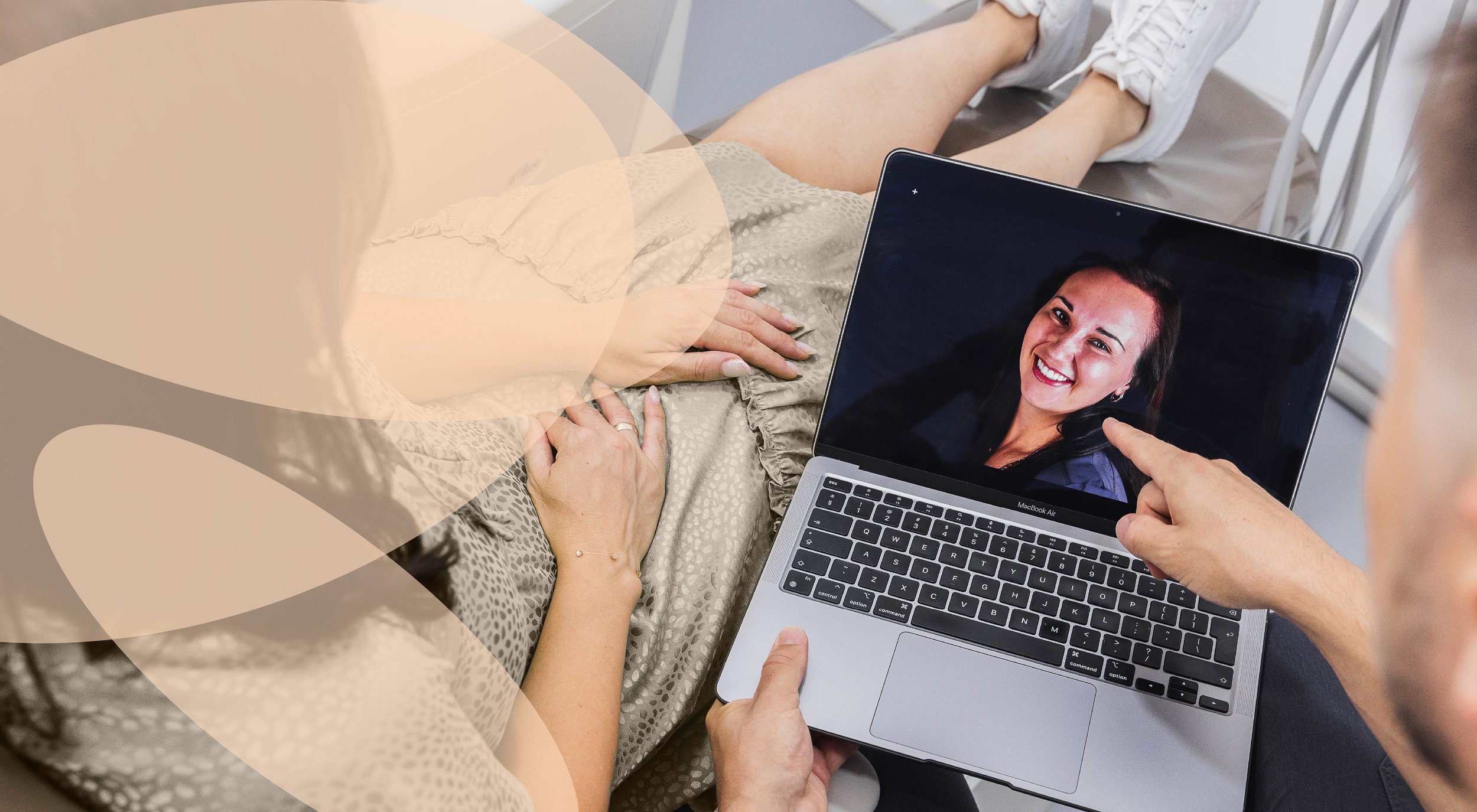 A person sitting in a chair holding a laptop that displays a smiling woman. The person has one hand on their lap and the other holding the laptop.