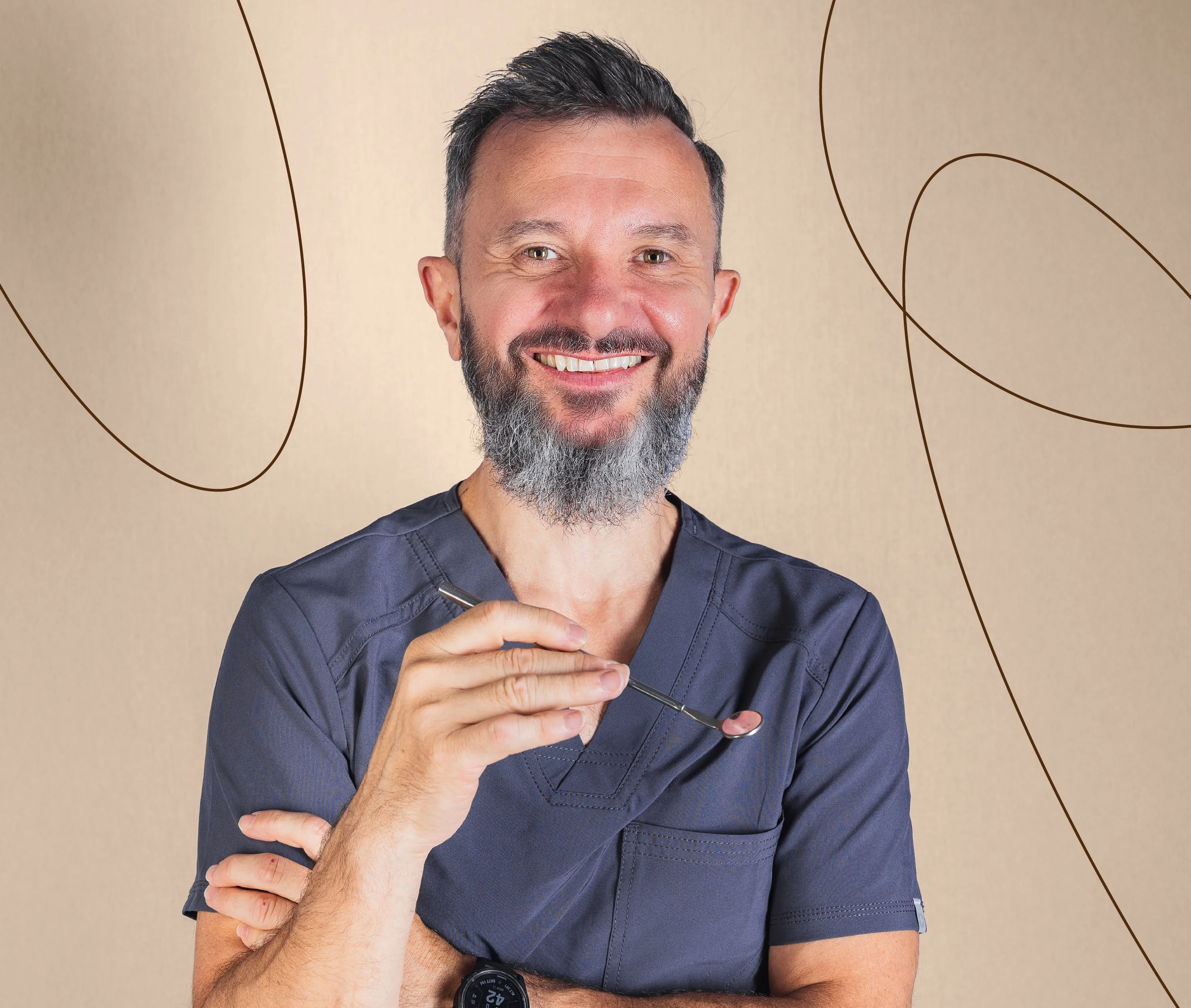 A smiling man with a beard, wearing dark gray medical scrubs, holding a dental mirror.