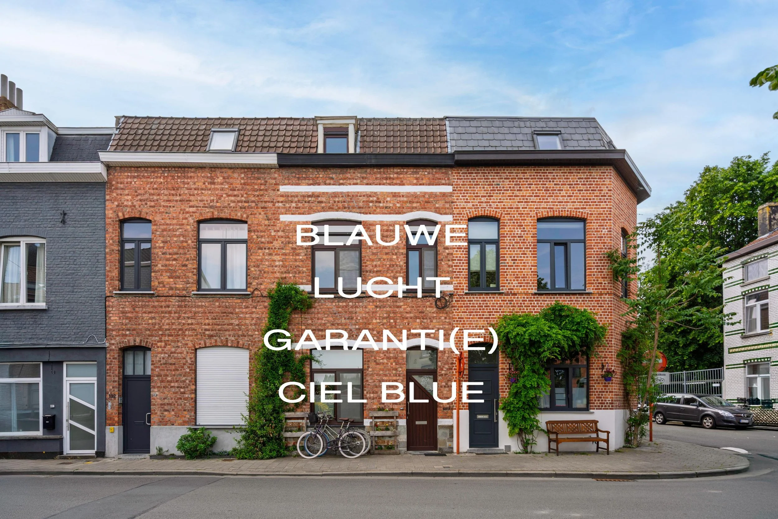 Traditioneel Nederlandse rijtjeshuis met gevel van rode baksteen, groene planten en fietsen voor de deur, onder een blauwe lucht.