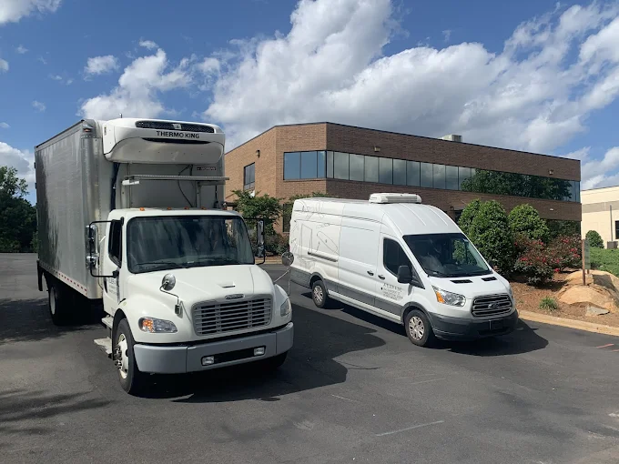 White delivery trucks parked in front of a modern office building with large glass windows and landscaped bushes.