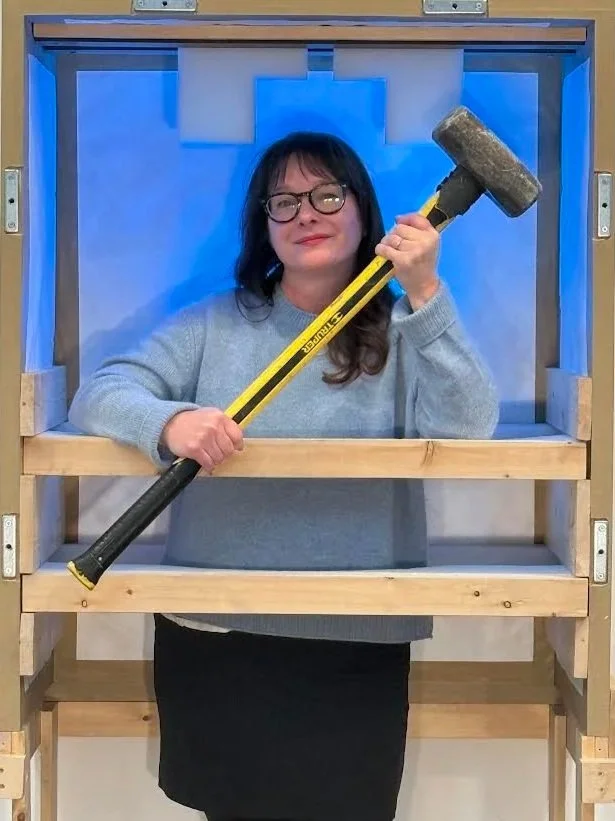 A wooden crate with red cut-out symbols and the words 'ATELIER 4' printed on it. The symbols include arrows pointing up, a hand with a wrench, and a hand holding a lightning bolt. There is also text that says 'OPEN THIS SIDE'.