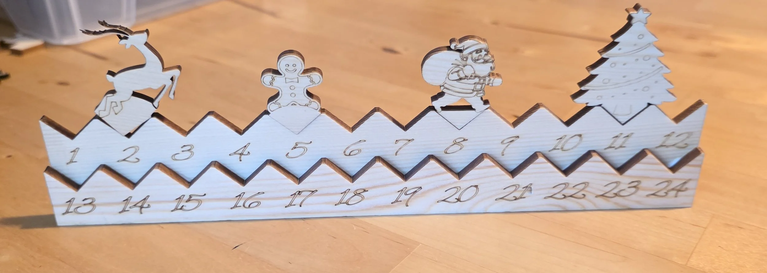 Wooden Advent calendar with 24 numbered zigzag steps, topped with holiday-themed figurines including a reindeer, gingerbread person, Santa Claus, and Christmas tree.