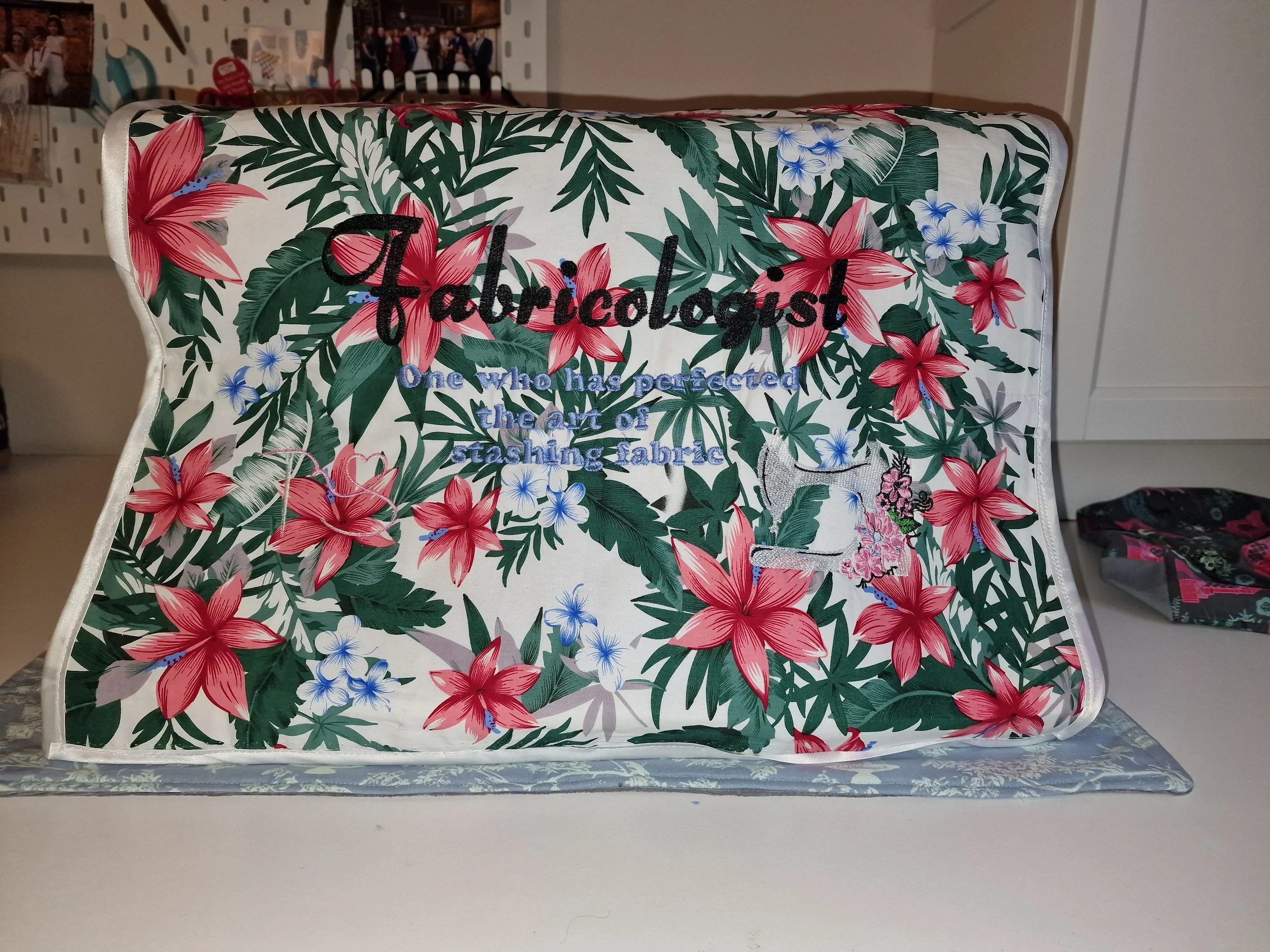 Patterned fabric with pink and green floral design and embroidered text that reads 'Fabricologist: One Who Has Perfected the Art of Brewing Fabric'.