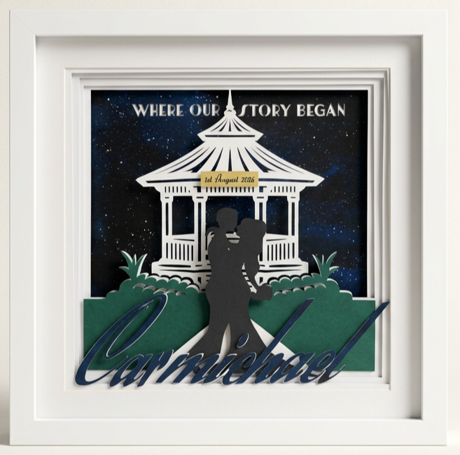 A decorative 3D wedding shadow box with a starry background, featuring a silhouette of a couple kissing, a gazebo, and the words 'Carmichael' and 'Where our story began' with a date label.